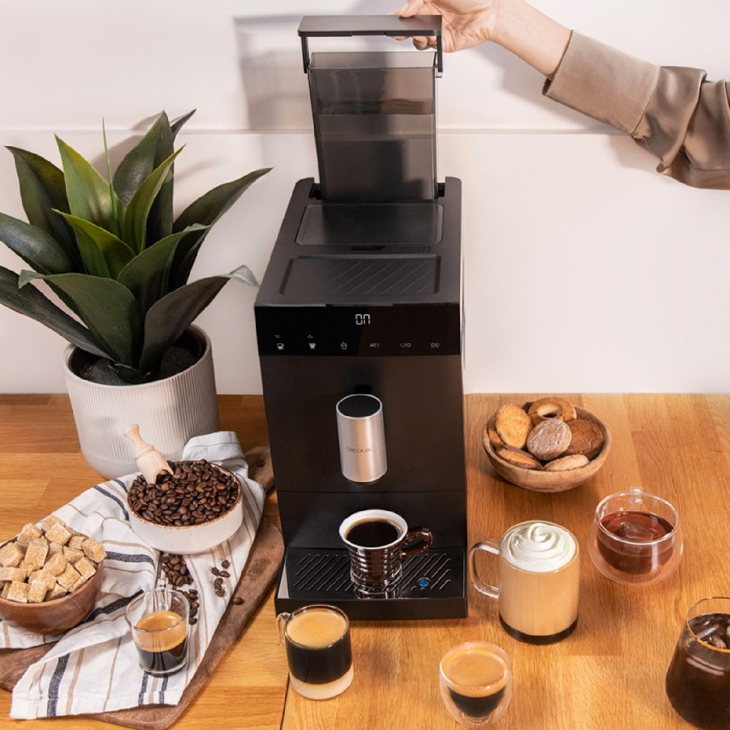 Una macchina da caffè con tazze, chicchi e pasticcini su un tavolo.