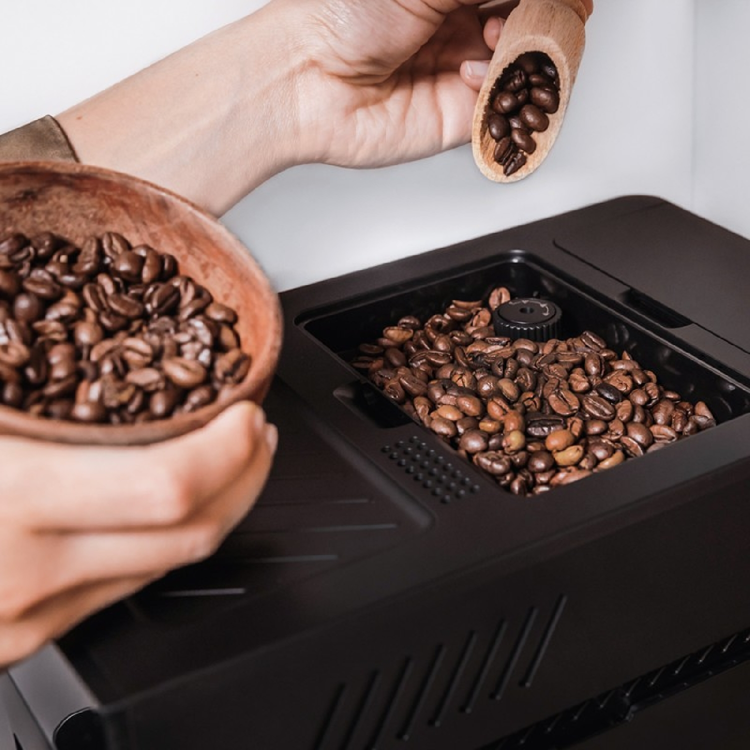 Persona che versa chicchi di caffè in una macchina da caffè. Ciotola e paletta di legno in mano.