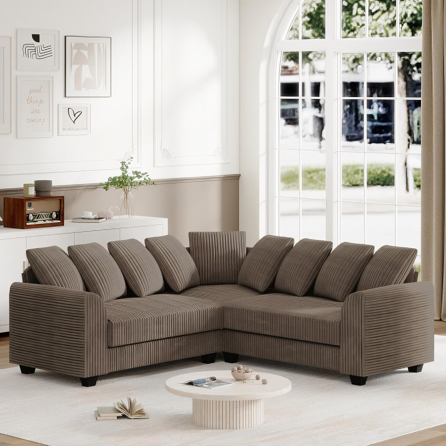Ein braunes Ecksofa mit Kissen, einem weißen Tisch und einem Fenster mit Vorhängen.