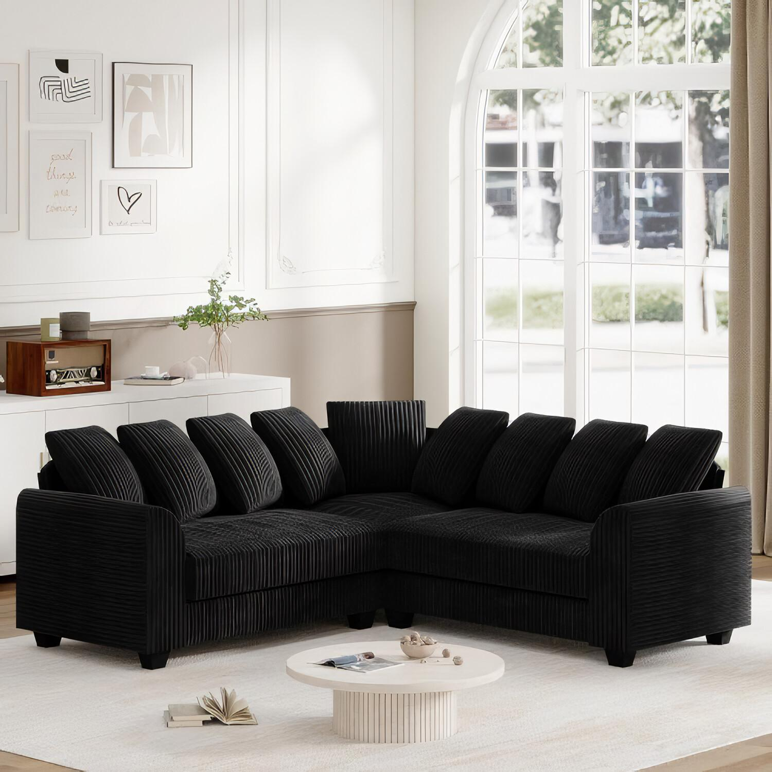Schwarzes Ecksofa mit Kissen und weißem Teppich. Dekoration und weißer Schrank im Hintergrund.