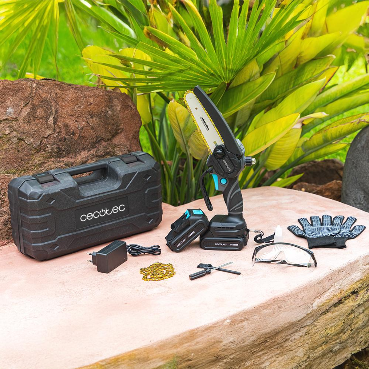 Un kit de herramientas en una superficie de hormigón. Incluye motosierra, baterías, cargador, guantes y equipo de protección.