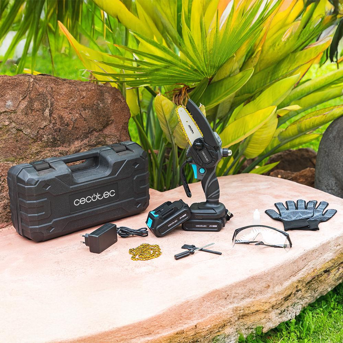 Pequeña motosierra negra con accesorios sobre una superficie de piedra. El fondo incluye una funda negra y plantas.