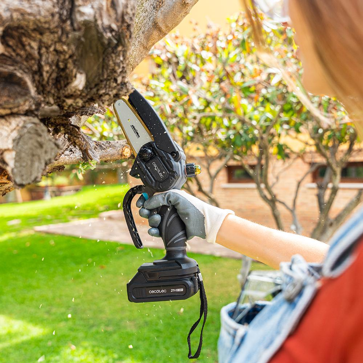 Una persona usa una pequeña motosierra negra para cortar una rama de árbol, en un patio trasero con césped.