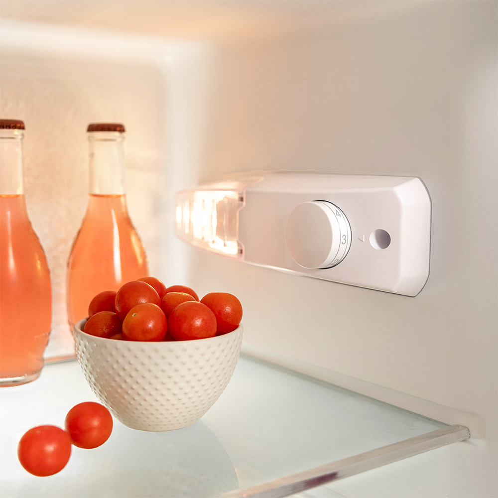 Dentro de un refrigerador con dos botellas y un tazón de tomates junto a la luz.