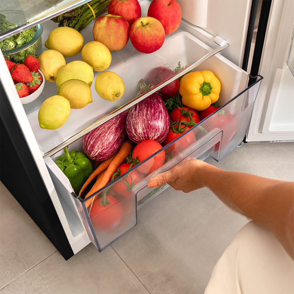 Un cajón de refrigerador lleno de verduras. Una mano está entrando para agarrar algo.