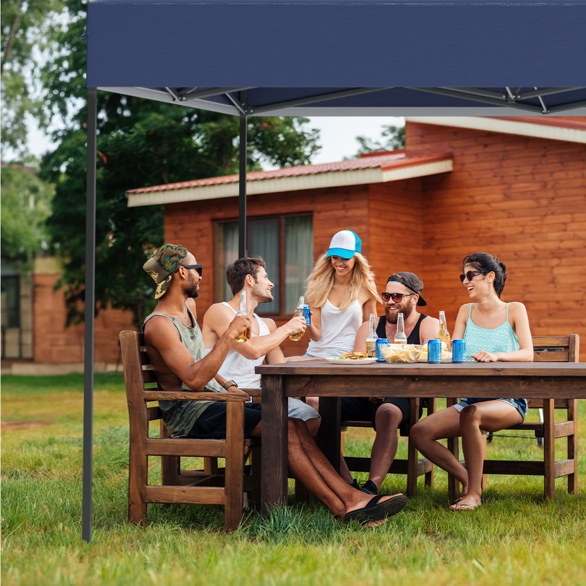 Group of five people under a blue tent, sitting at a wooden table, enjoying drinks and food.