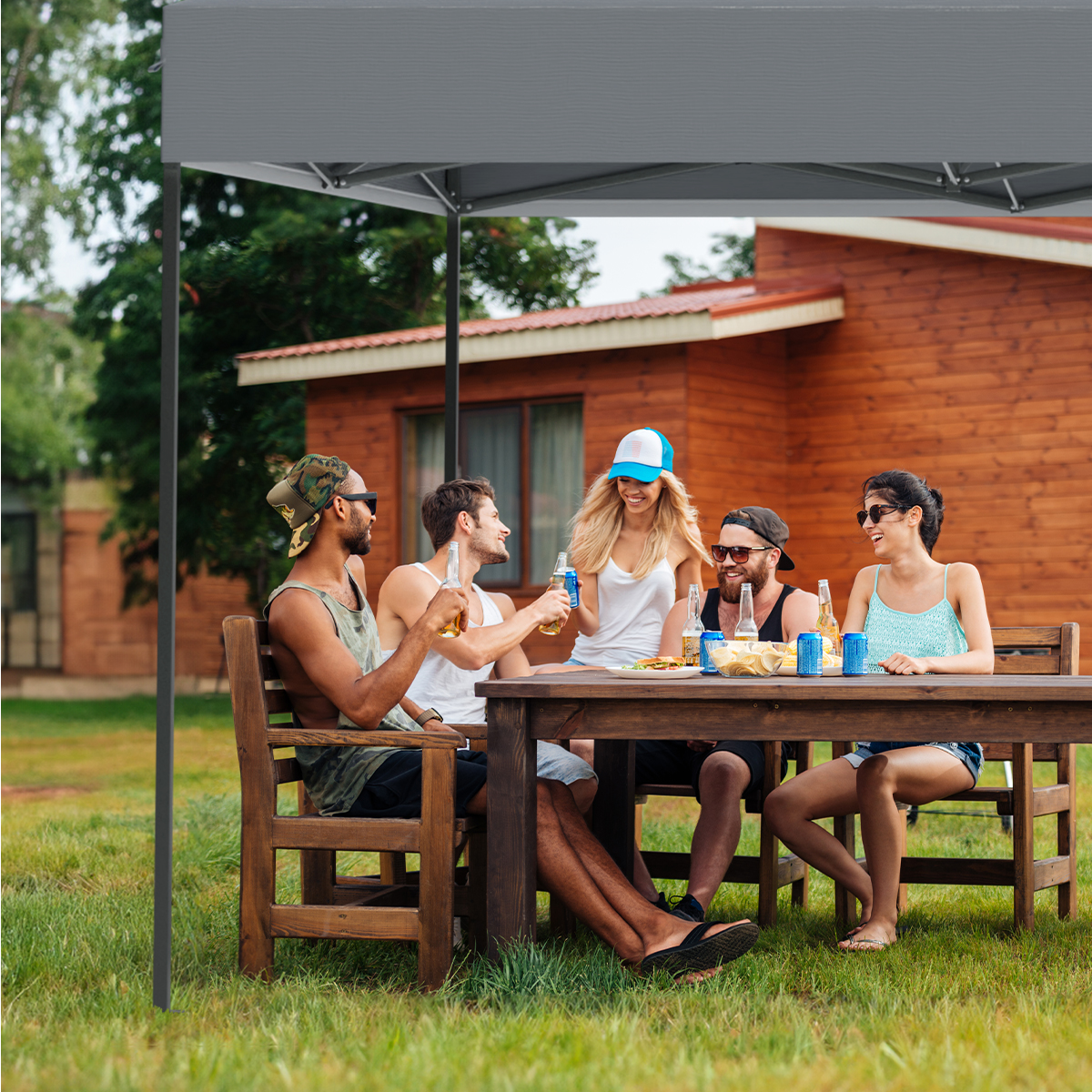 Five people sitting at a table under a grey canopy tent, enjoying drinks and conversation.