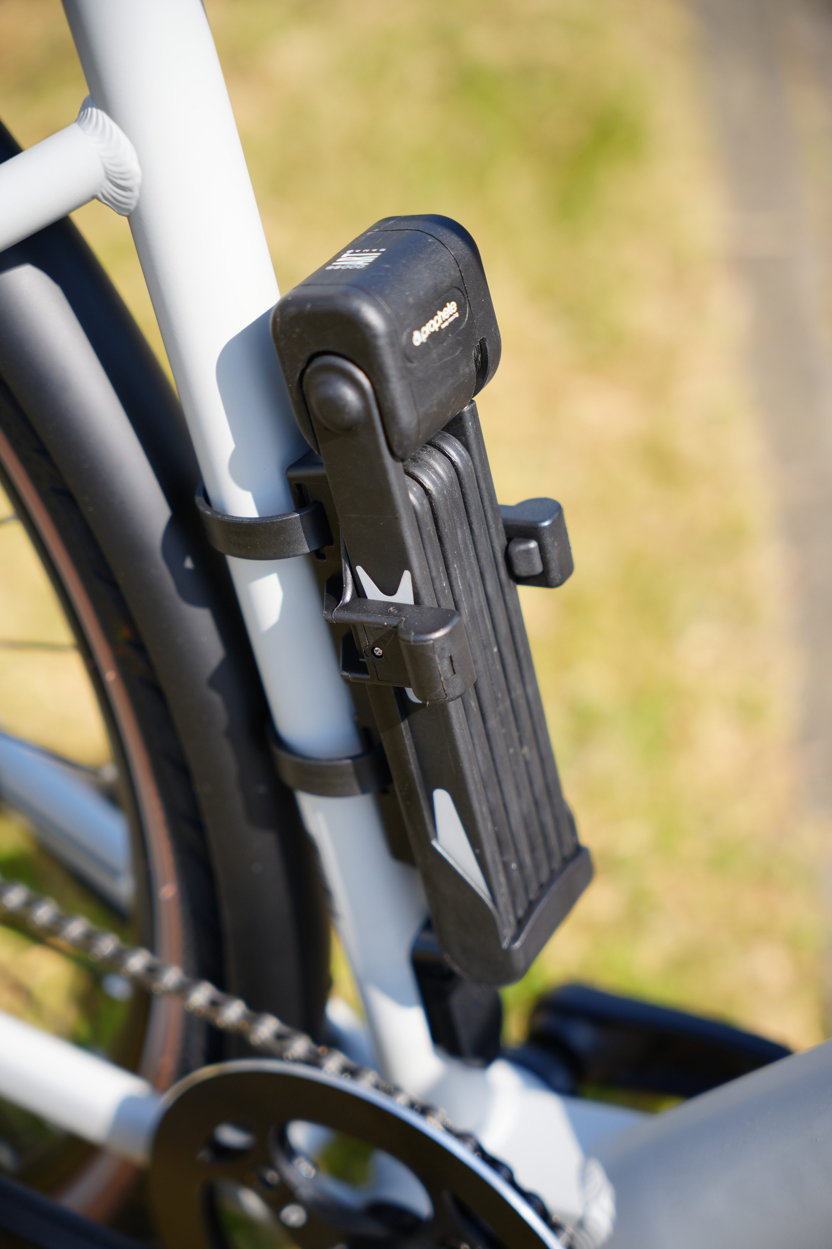 Nahaufnahme eines Fahrrads mit einem zusammengeklappten Schloss am Rahmen. Das Fahrrad steht auf einem grasbewachsenen Weg.