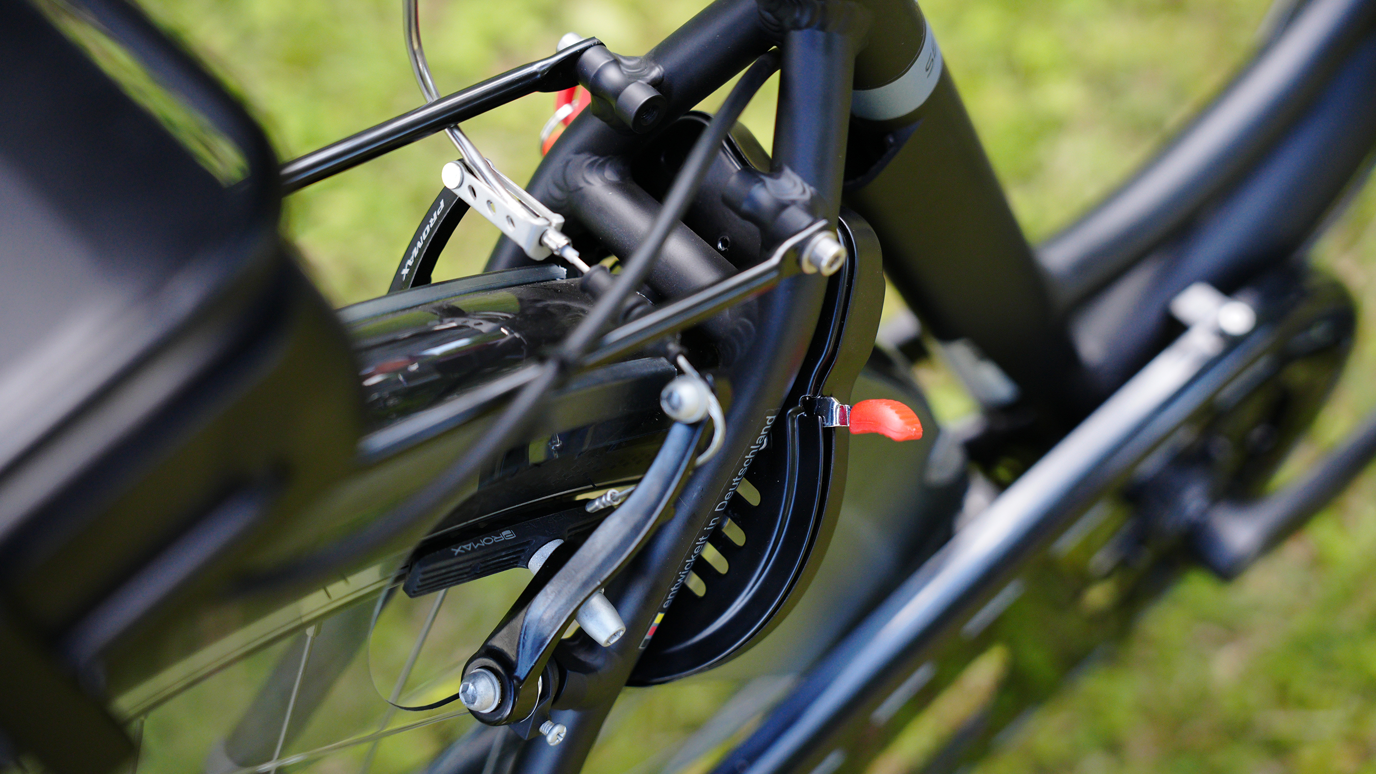 Nahaufnahme eines schwarzen Fahrradbremssystem. Das Bremskabel und die Teile sind sichtbar. Der Hintergrund ist grünes Gras.