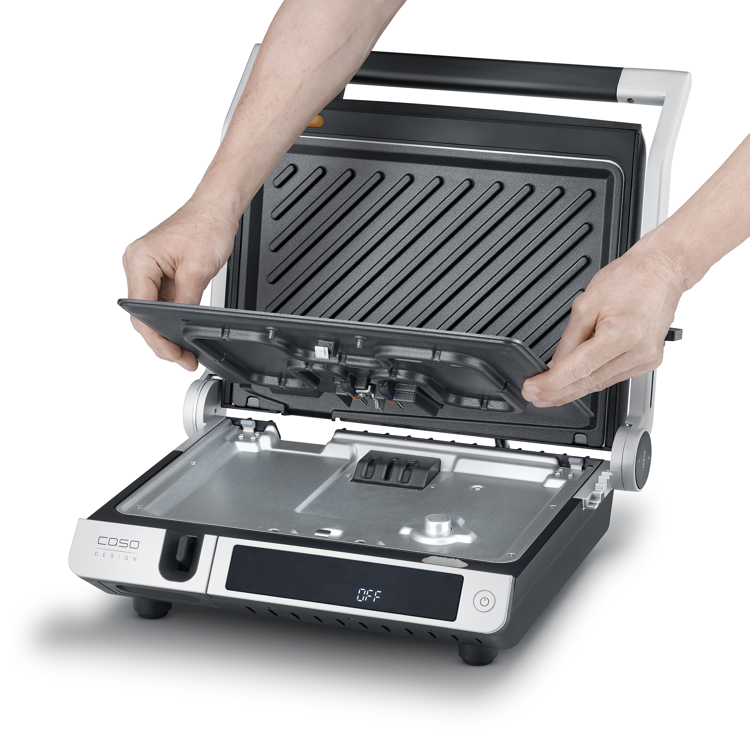 Hände legen eine Grillplatte auf einen schwarzen und silbernen Grill. Der Grill hat eine OFF-Anzeige und steht auf einer weißen Fläche.