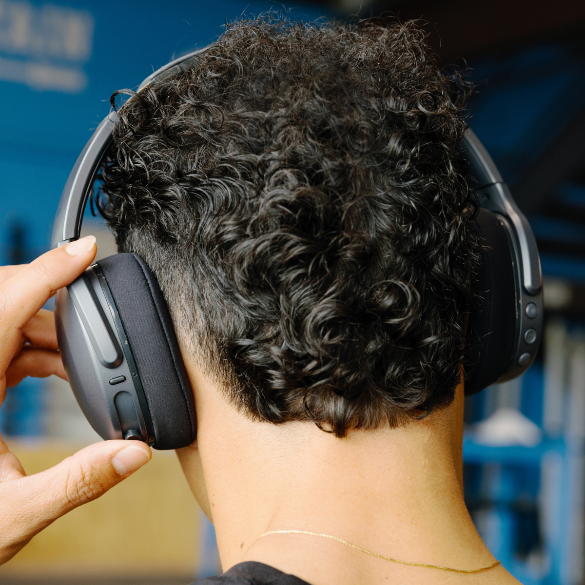 Osoba z tyłu w czarno-szarych słuchawkach. Widoczny złoty naszyjnik.