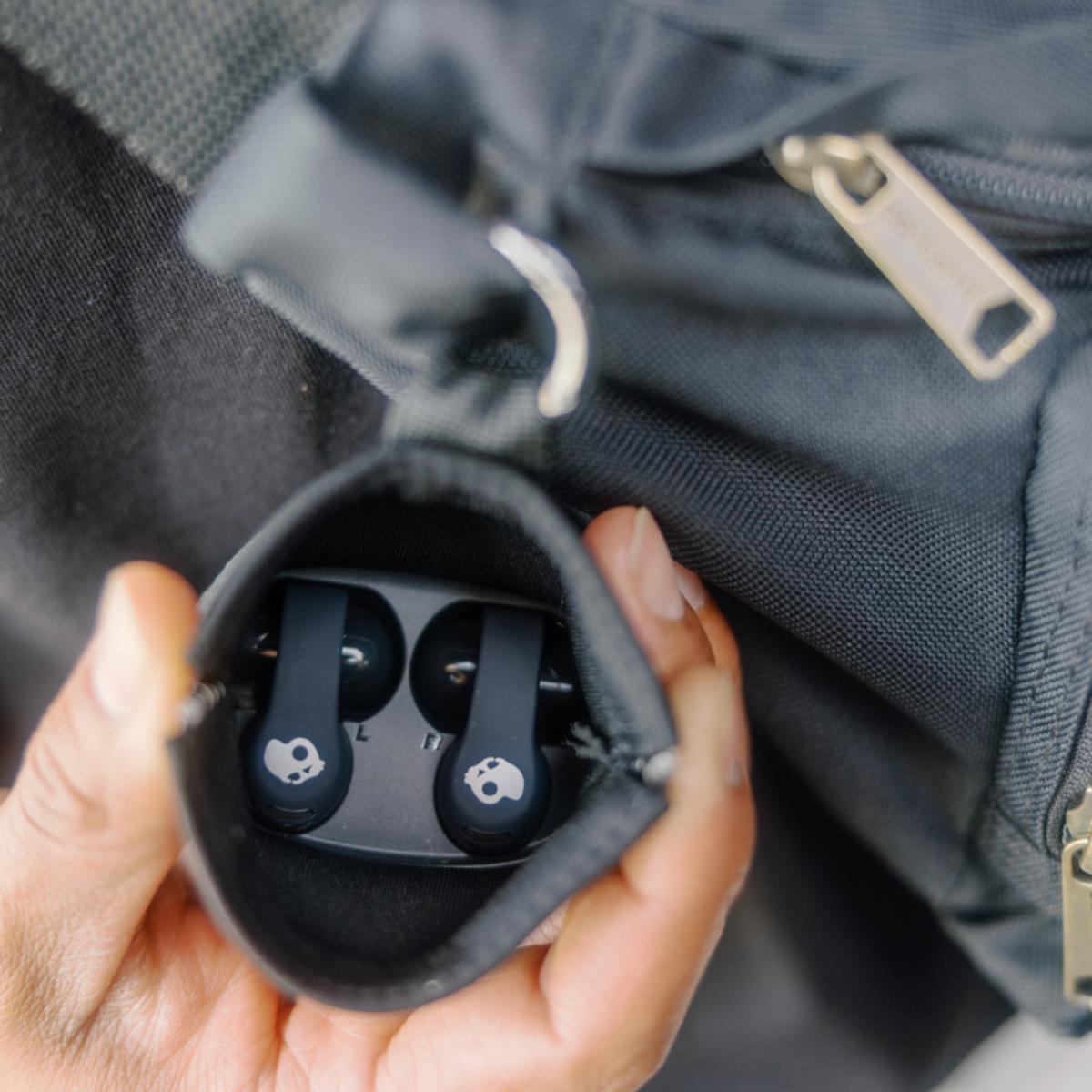 Una mano tiene una custodia nera con auricolari all'interno. La custodia è dentro una borsa nera.