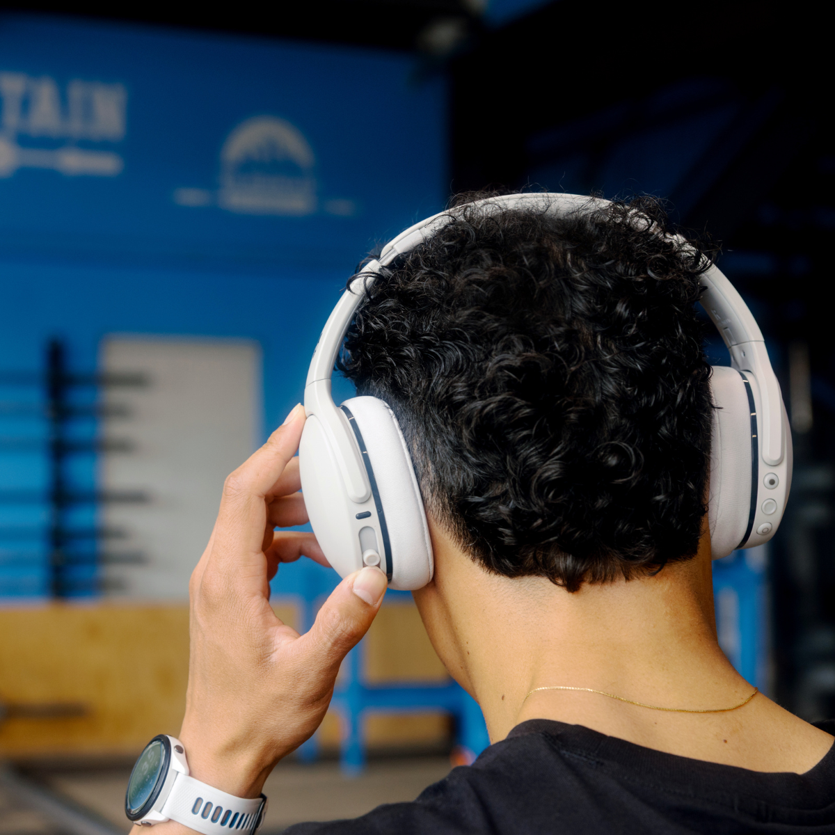 Osoba nosząca białe słuchawki i czarną koszulę. Plecy osoby skierowane są w stronę aparatu.