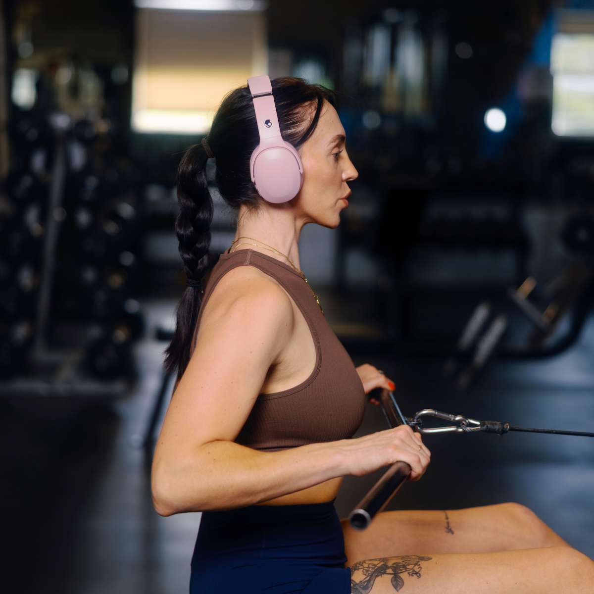 Kobieta w różowych słuchawkach podczas ćwiczeń. Ciągnie za maszynę z linkami.