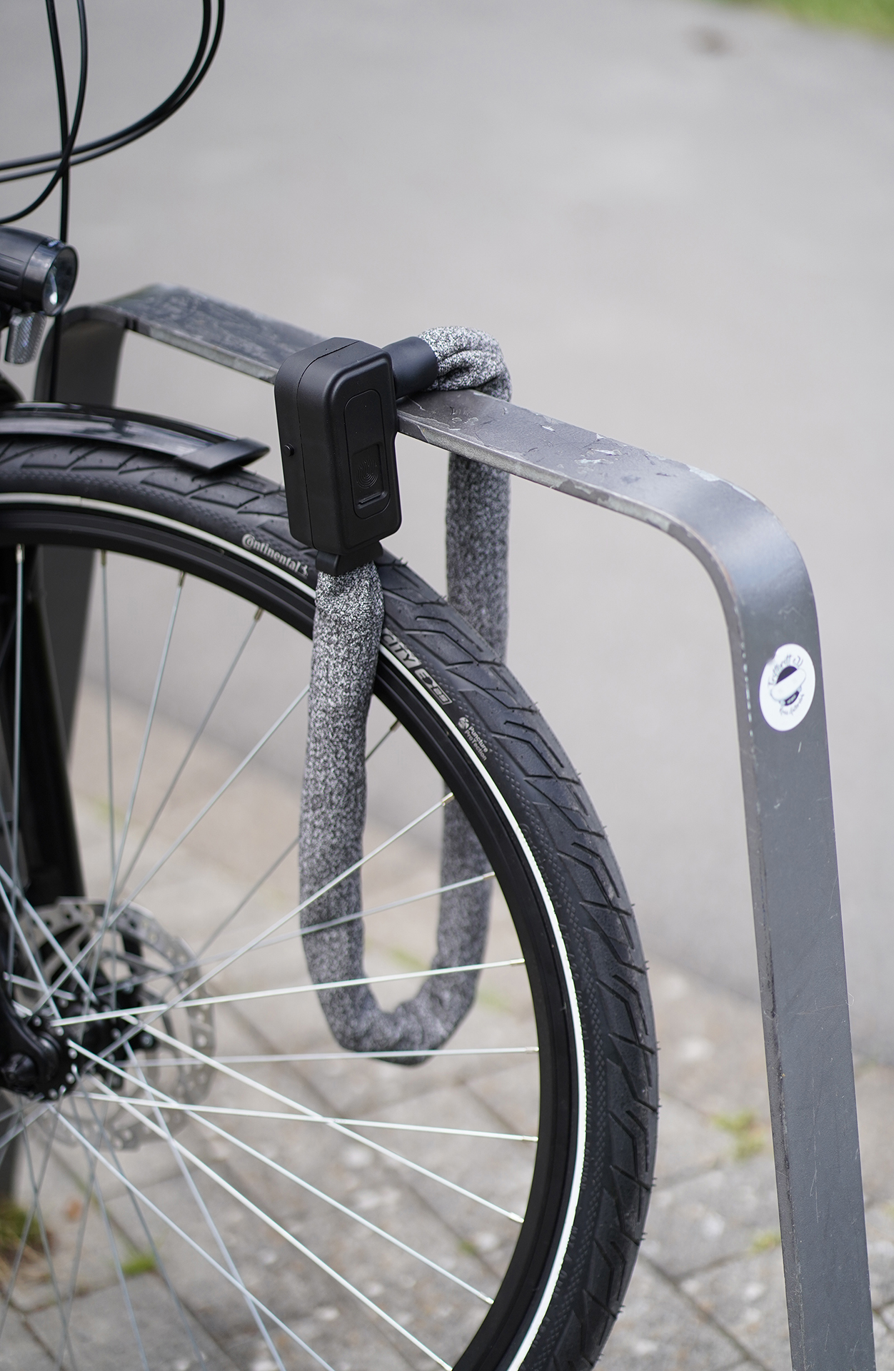 Ein Fahrrad ist mit einem Kettenschloss an einem Gestell gesichert. Das Schloss ist geschlossen und um das Hinterrad herum.