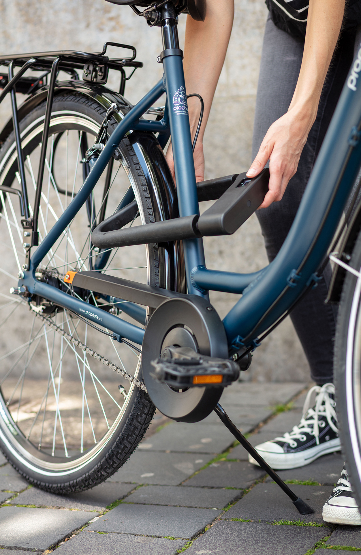 Eine Person sichert ein Fahrrad mit einem U-Schloss. Das Fahrrad ist blau, und die Person trägt Turnschuhe.