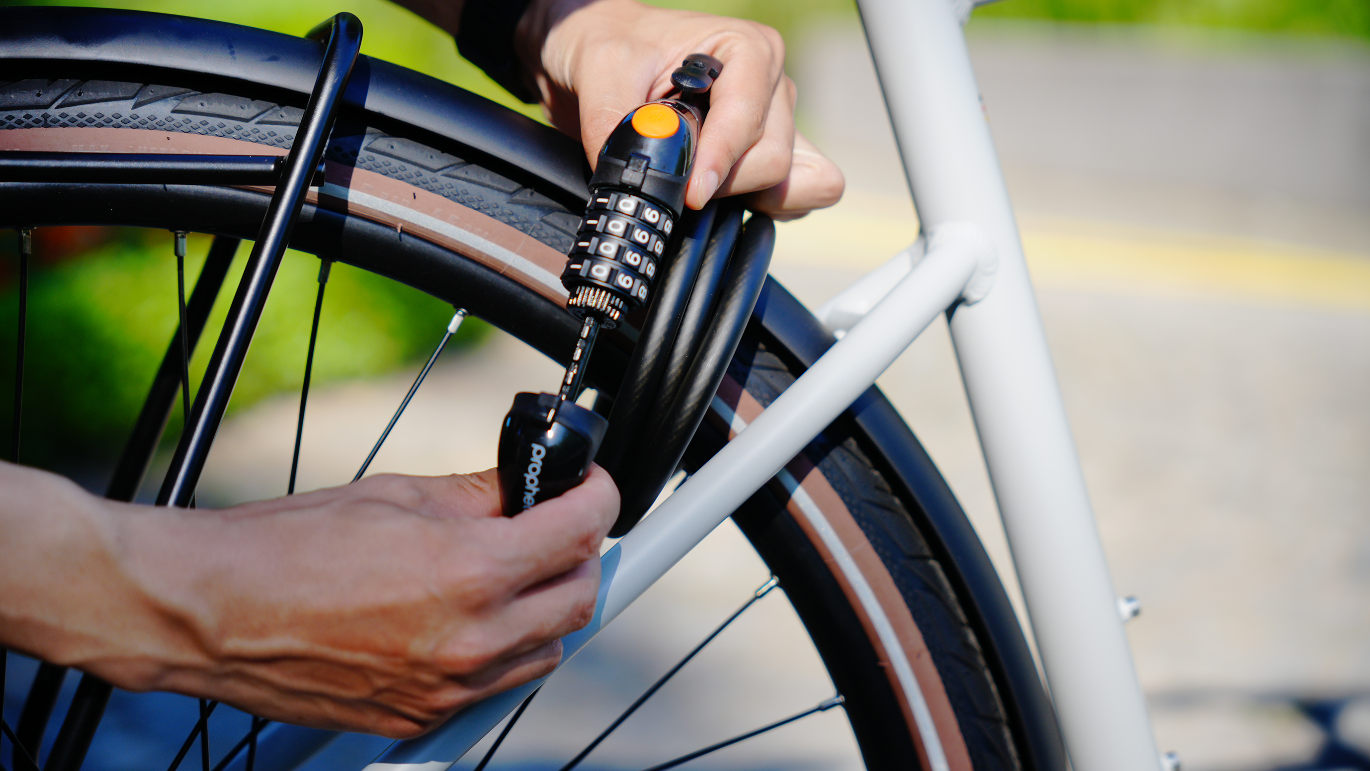 Hände einer Person, die ein schwarzes Fahrradschloss an einem Fahrradrahmen verriegeln. Nahaufnahme. Sonniger Tag.