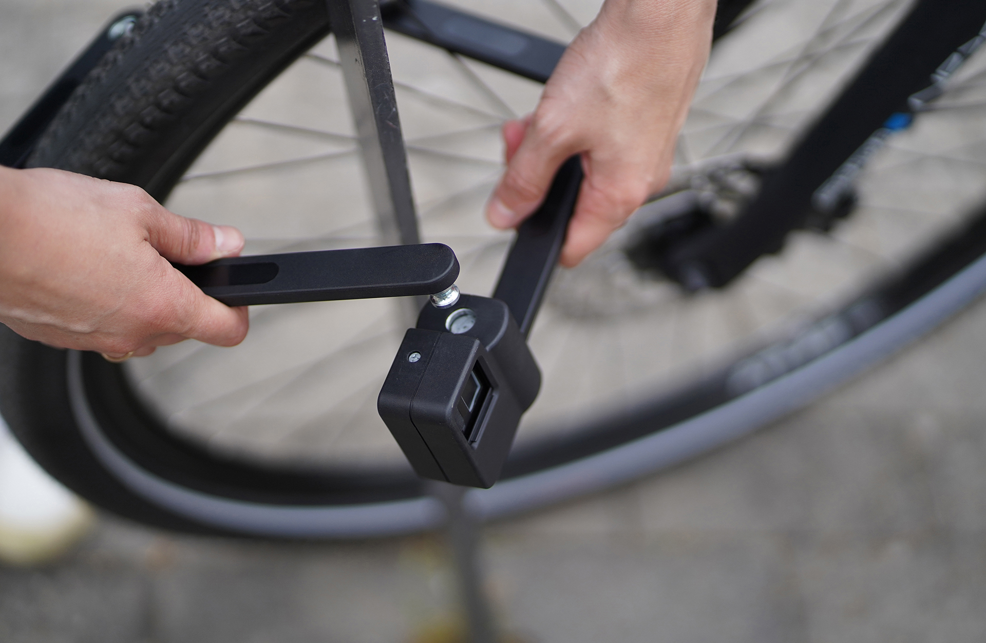 Hände befestigen ein schwarzes Fahrradschloss an einem Fahrradrad.