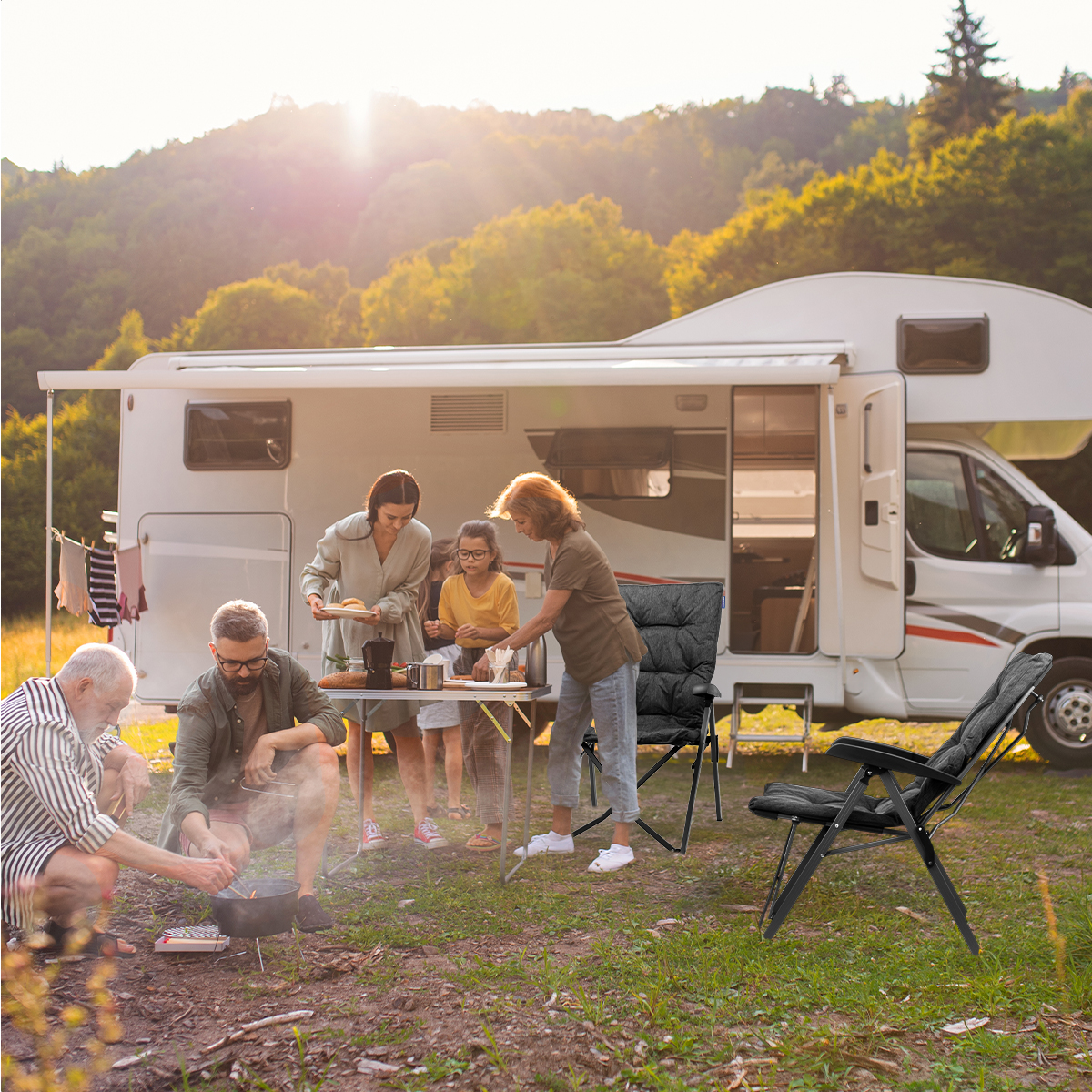 Family camping by a camper, cooking food. Chairs and a table are set up nearby. Sunny day.
