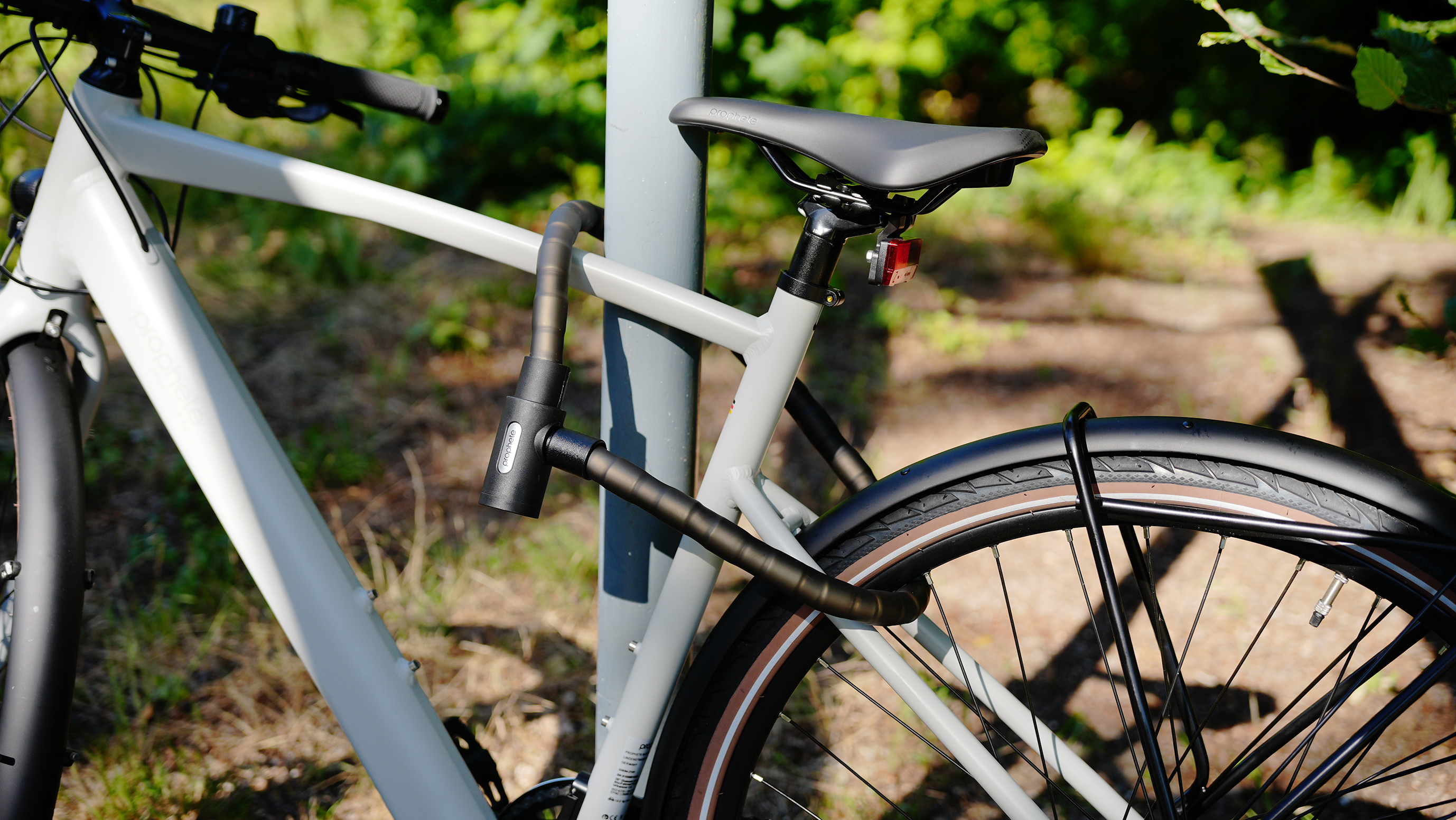Ein graues Fahrrad ist an einem Pfosten angeschlossen. Das Fahrrad hat schwarze Reifen und einen grauen Rahmen. Grüner Hintergrund.