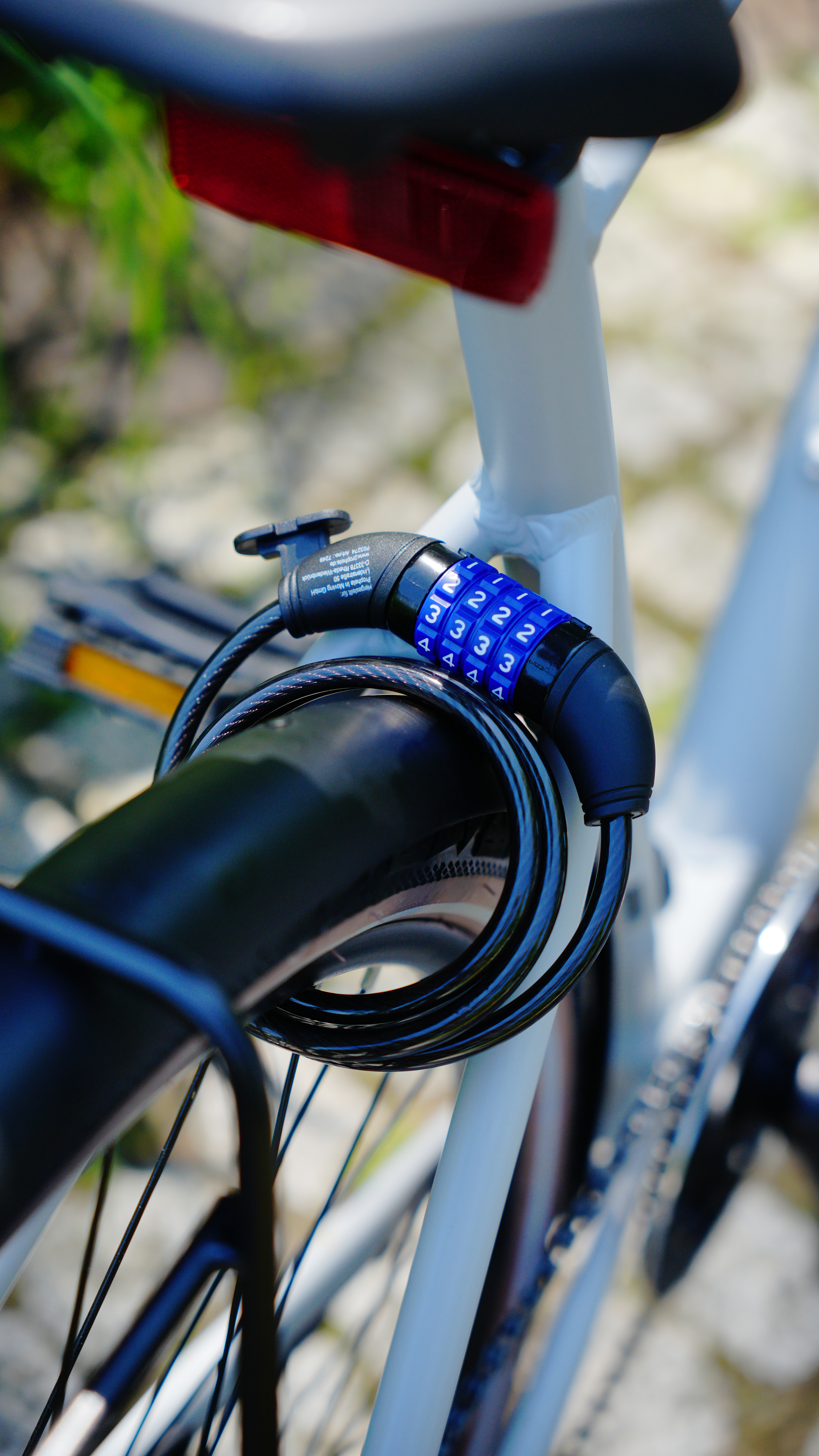 Ein Fahrradschloss mit der Kombination 3434 ist am Fahrrad befestigt. Ein roter Reflektor und Laub im Hintergrund.