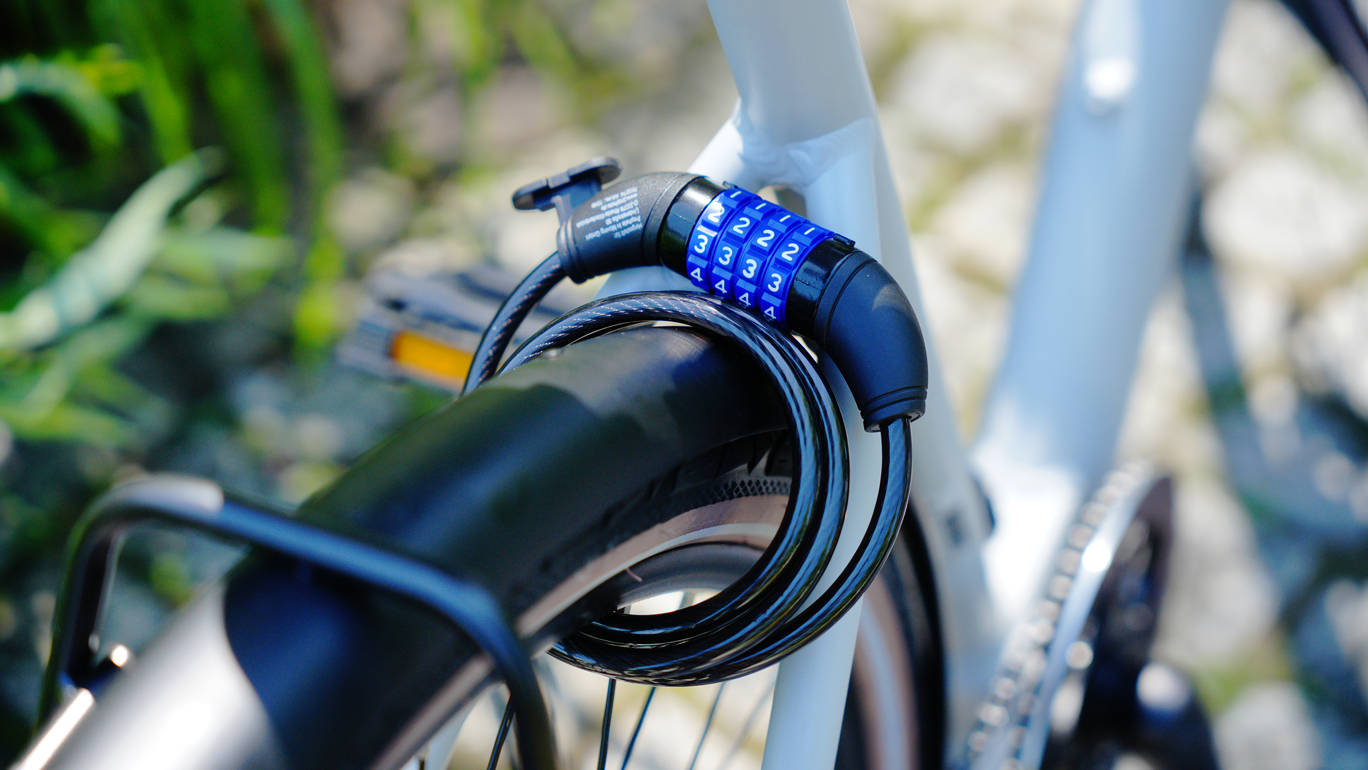 Ein Fahrradschloss mit der Kombination 2333 ist am Fahrradrahmen und am Rad befestigt. Grünes Laub im Hintergrund.