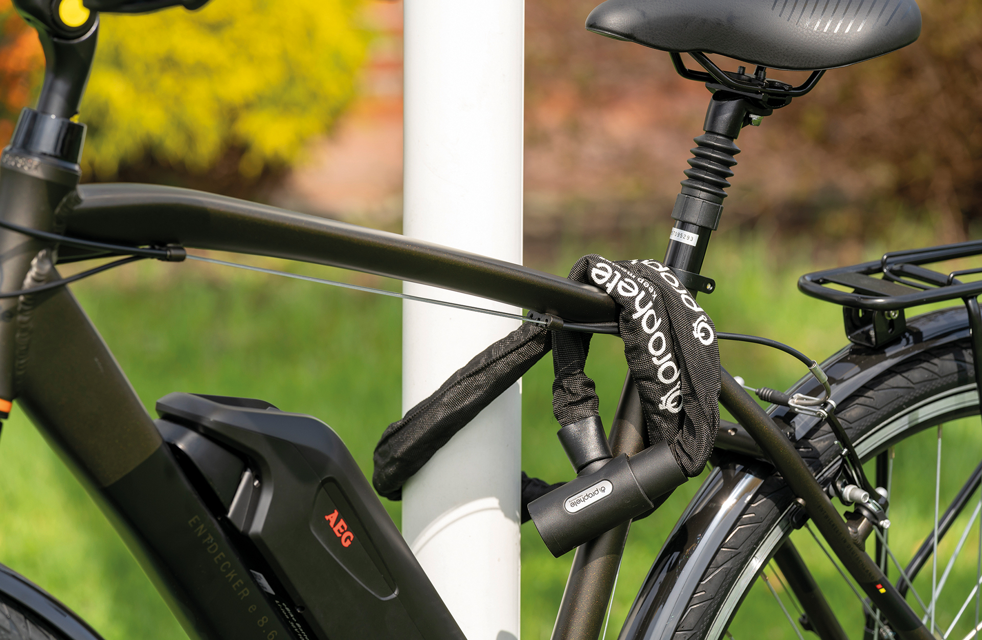Ein Fahrrad, das mit einem Kettenschloss an einem Pfosten befestigt ist. Das Fahrrad ist schwarz und grün, mit einem Akku und dem AEG-Logo.