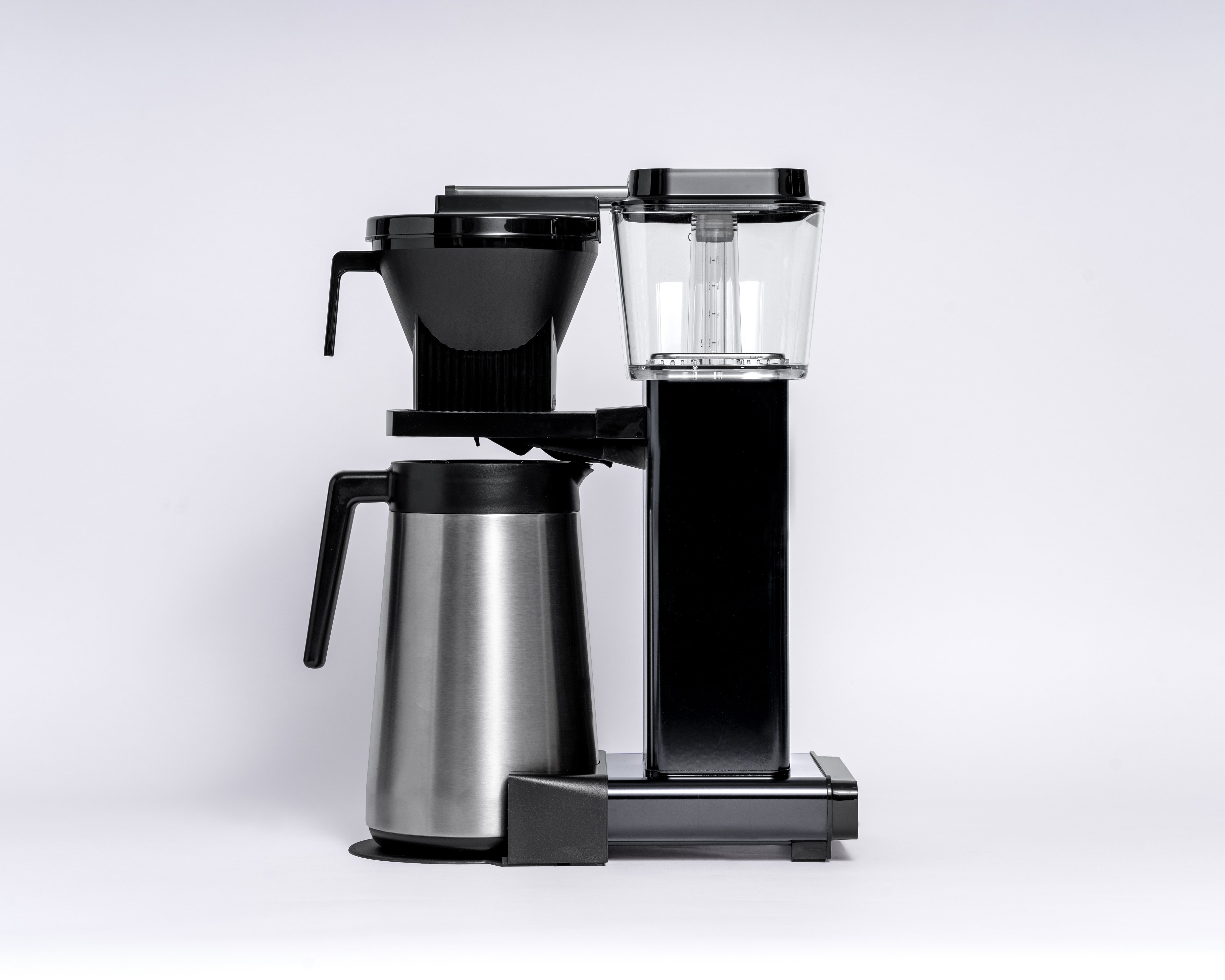 Czarny ekspres do kawy z karafką i przezroczystym zbiornikiem na wodę. Widok z boku, na białym tle.