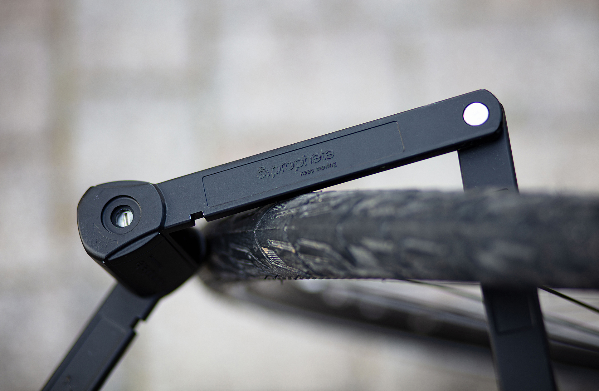 Ein schwarzes Fahrradschloss ist an einem Reifen befestigt, wobei der Markenname sichtbar ist. Der Hintergrund ist eine verschwommene graue Oberfläche.