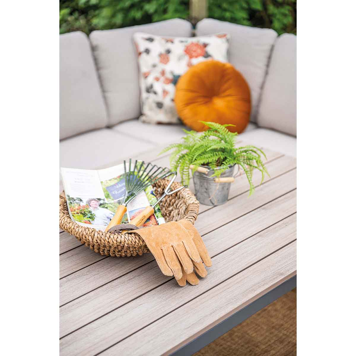 Une table avec des fournitures de jardinage : gants, un panier, une petite plante et des outils de jardinage. Un canapé est à l'arrière-plan.
