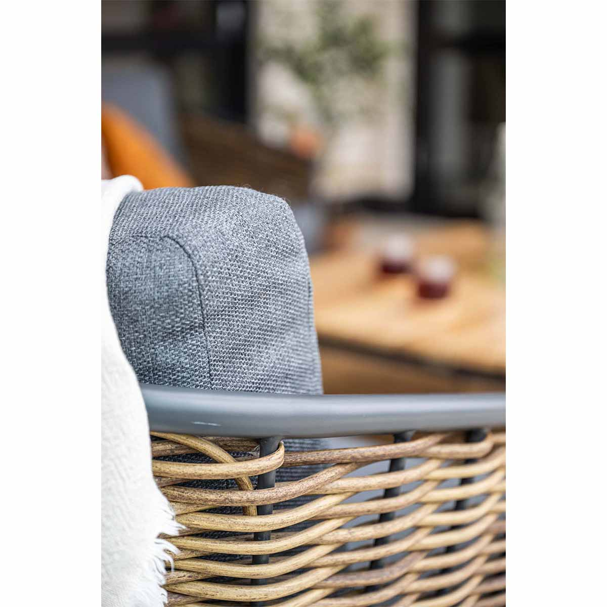 Close-up of a wicker chair with a gray cushion and a white blanket draped over the backrest.