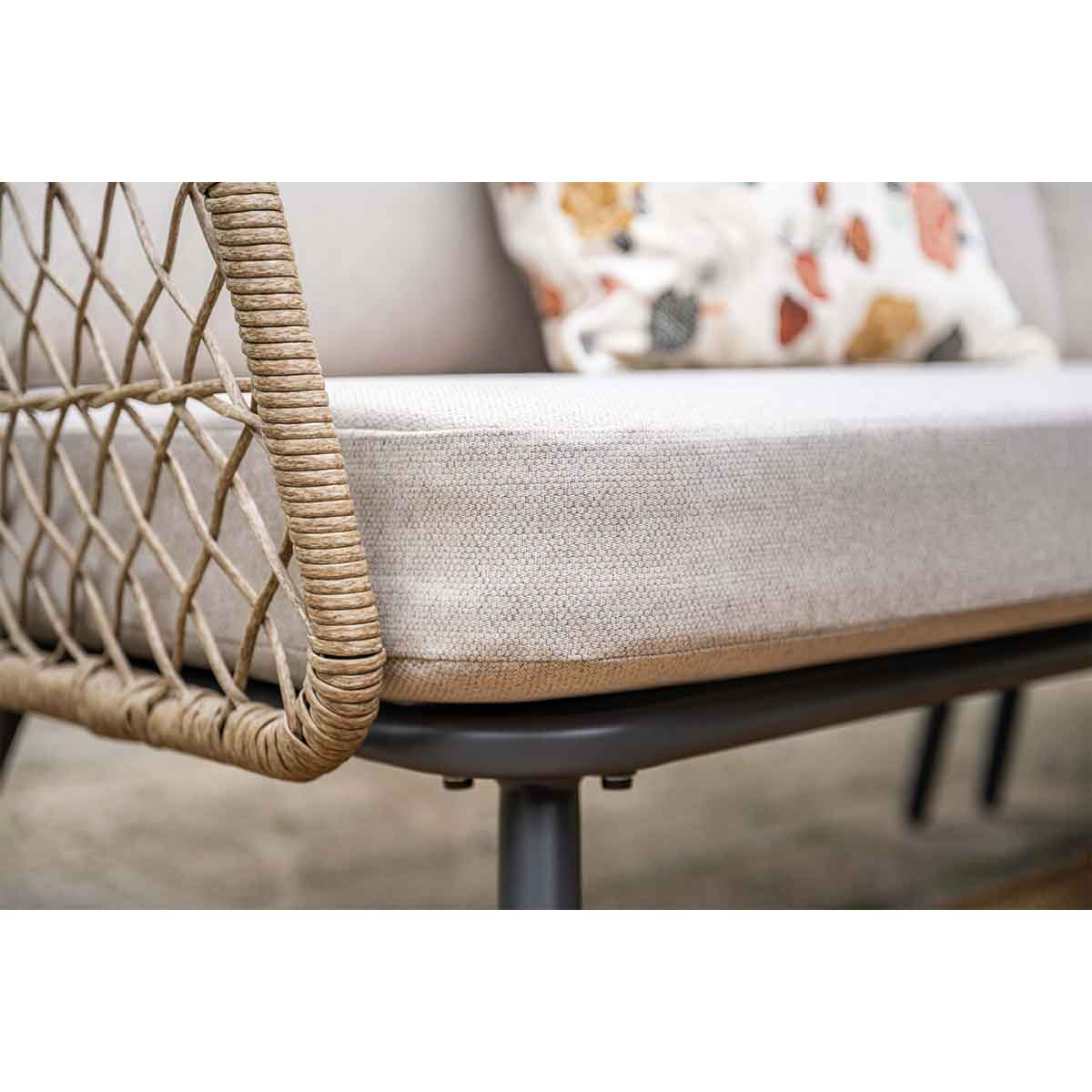 Un canapé avec un côté tissé et des coussins. Il repose sur une base sombre. La texture est visible. Cadre extérieur.