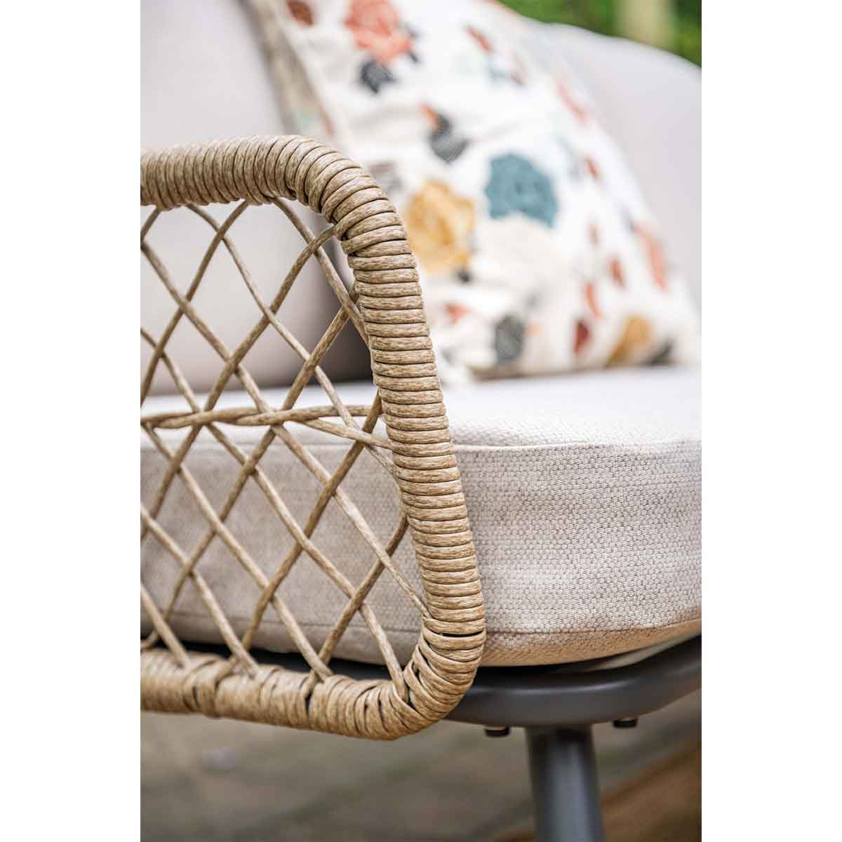 Gros plan d'un côté tissé marron d'un canapé d'extérieur. Coussin beige et oreiller floral sont visibles.