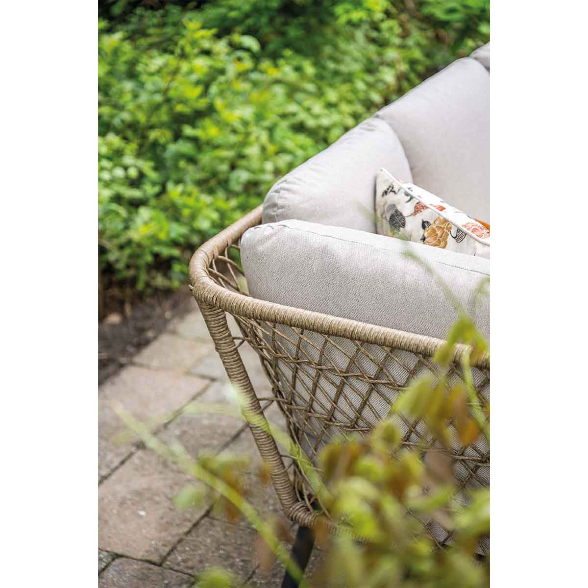 Gros plan d'un côté tissé marron d'un canapé d'extérieur. Coussin beige et feuillage vert en arrière-plan.