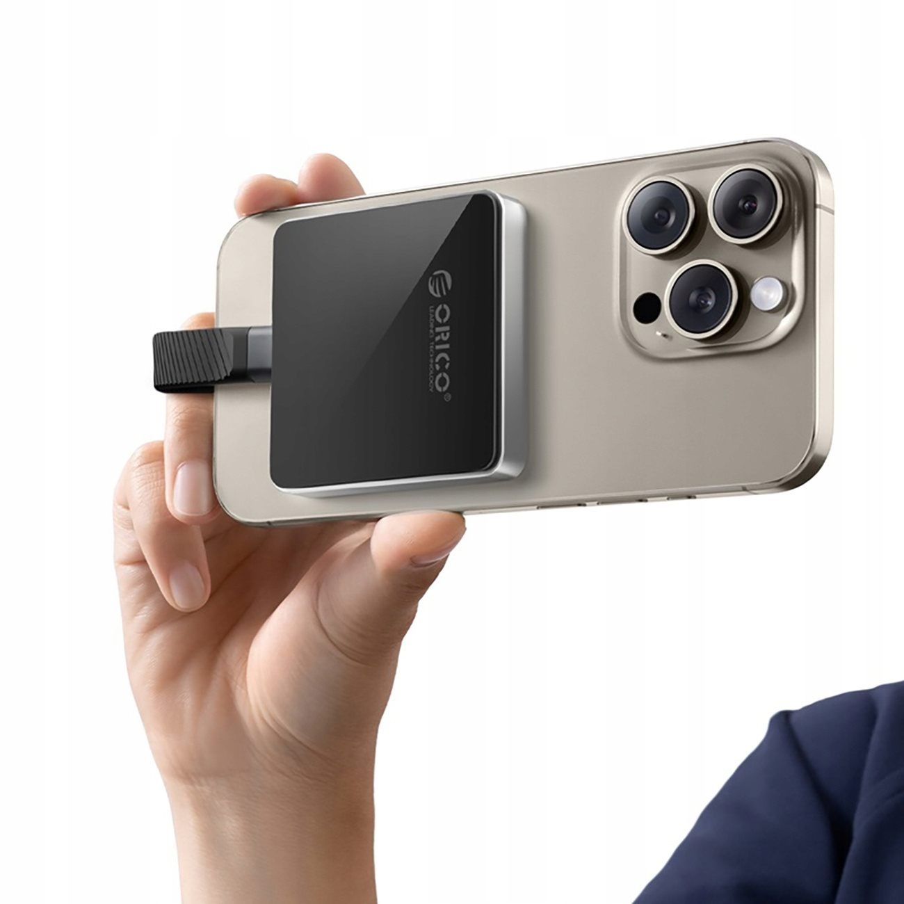 Ręka trzyma telefon z czarną ładowarką magnetyczną; ładowarka ma logo Orico.