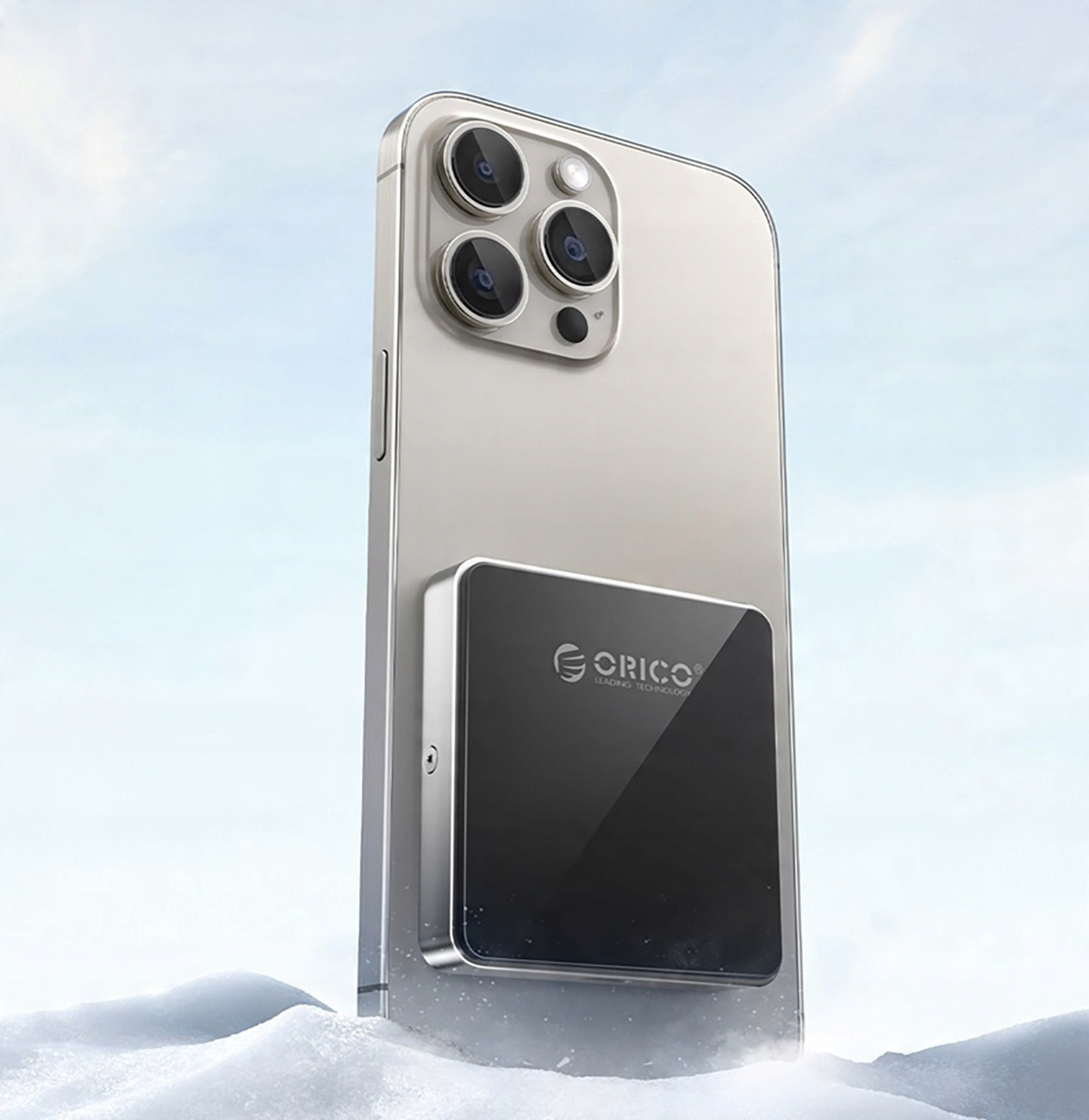 Telefon z czarną ładowarką magnetyczną, tło śnieżne, ładowarka ma logo Orico.