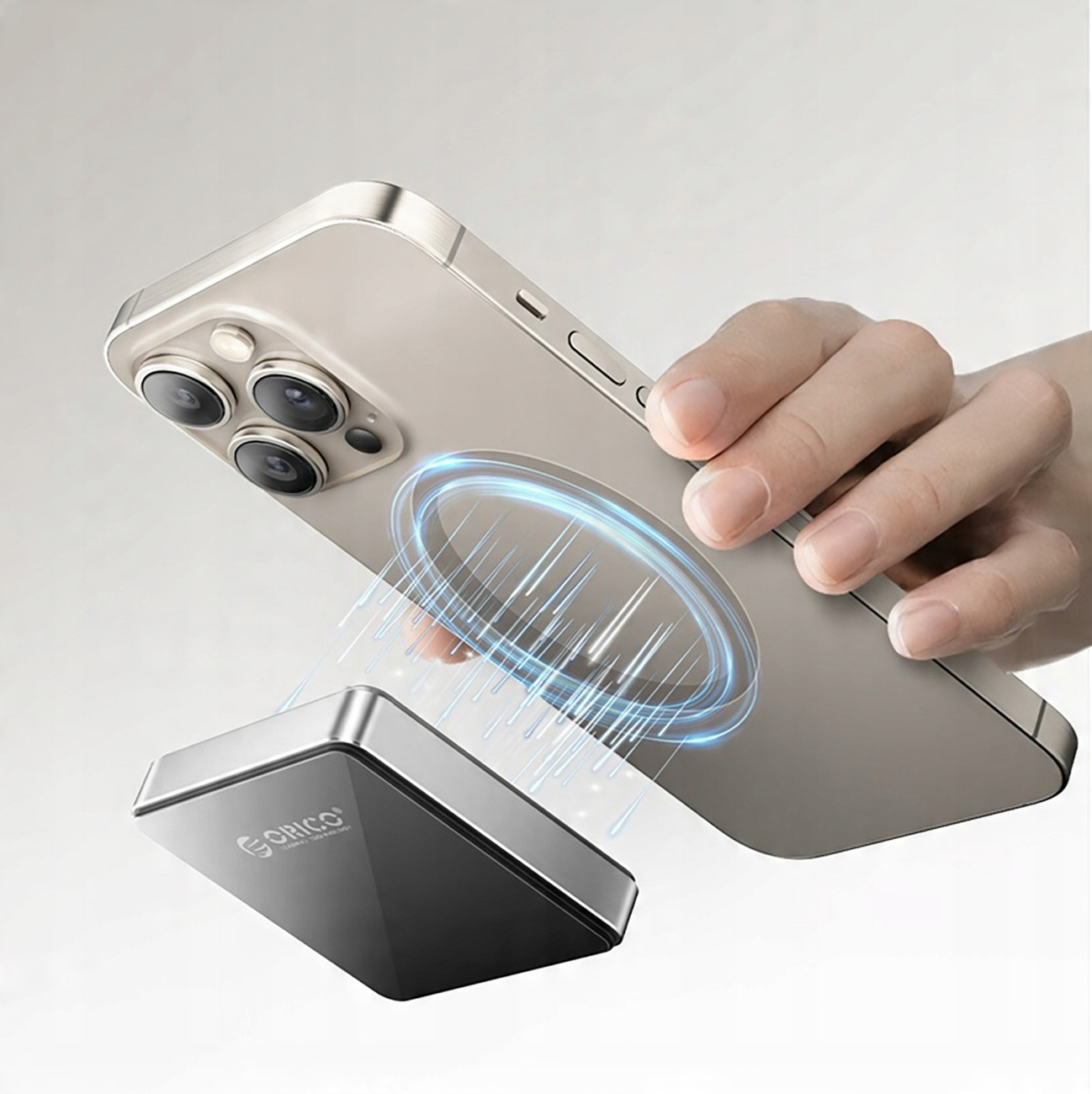 Telefon z ładowarką magnetyczną. Ręka trzyma telefon. Ładowarka jest srebrna i czarna.