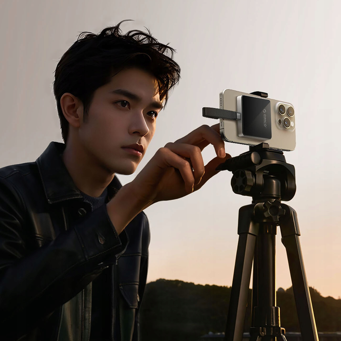 Mężczyzna ustawia telefon na statywie. Telefon ma magnetyczną ładowarkę Orico.