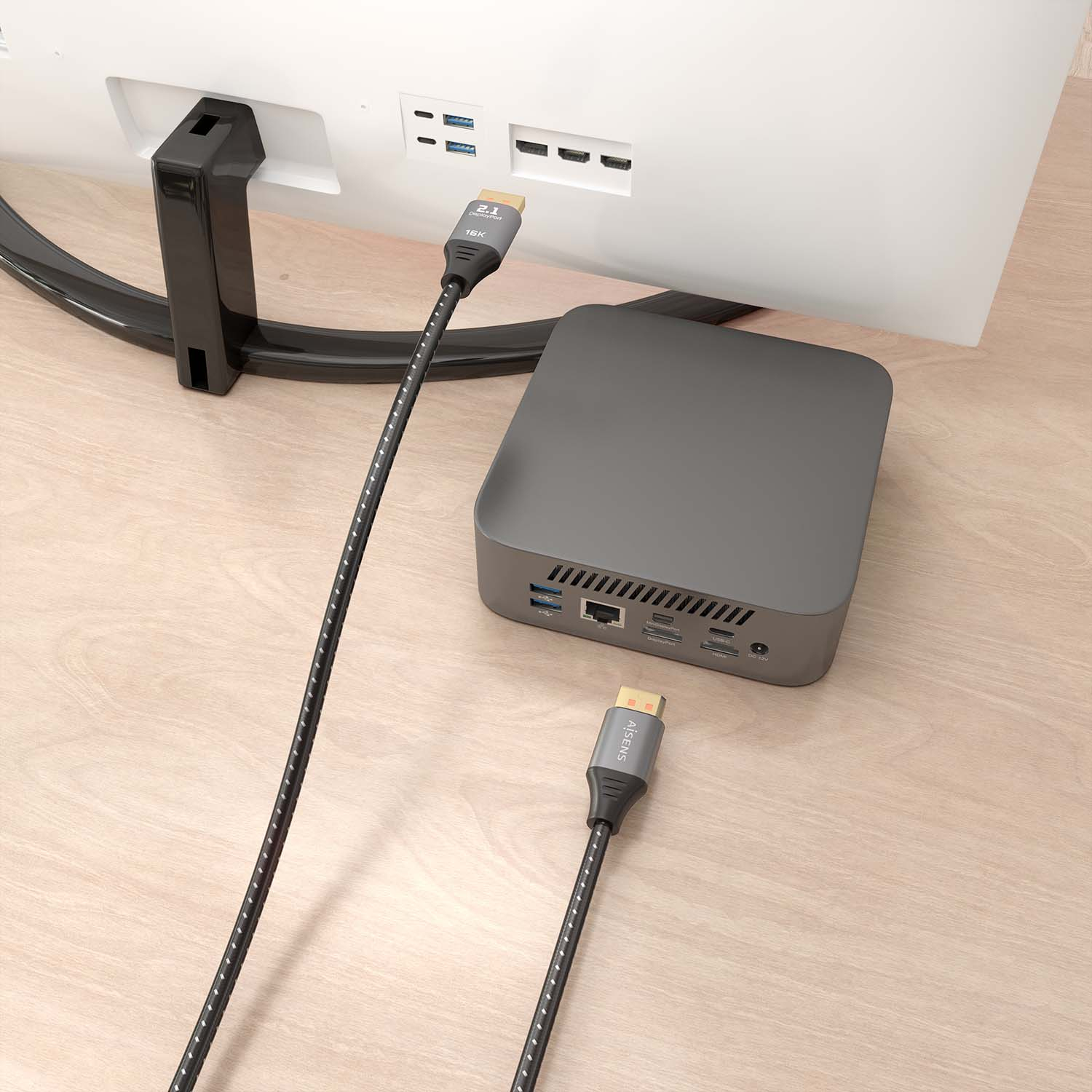 Een HDMI-kabel aangesloten op een monitor en een klein zwart apparaat, op een houten bureau.