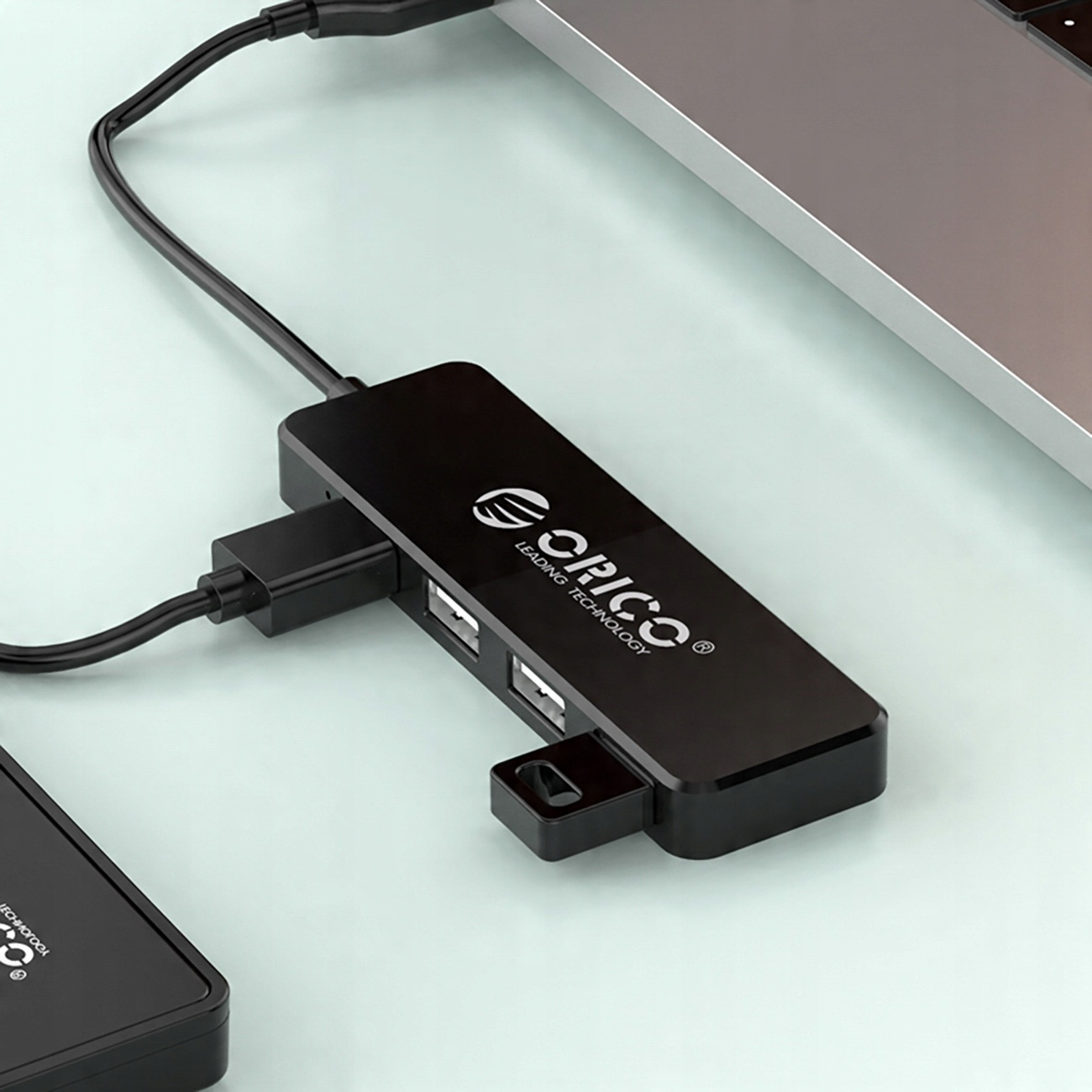 Czarny hub USB podłączony do laptopa, z marką 'ORICO' na powierzchni.