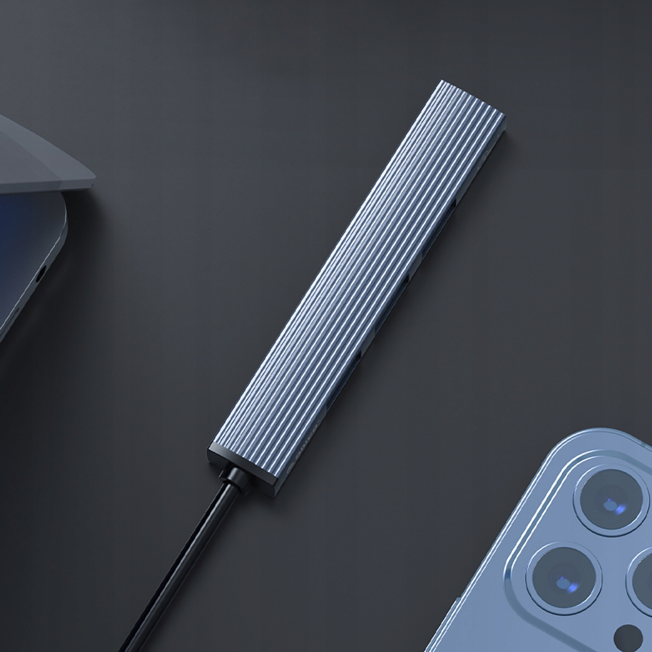 Srebrny hub USB z czarnym kablem i smartfonem. Hub ma niebieskie światło.