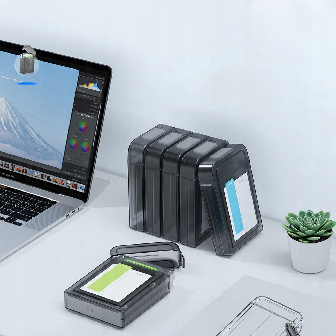 Obudowy dysków twardych na biurku z laptopem i rośliną.