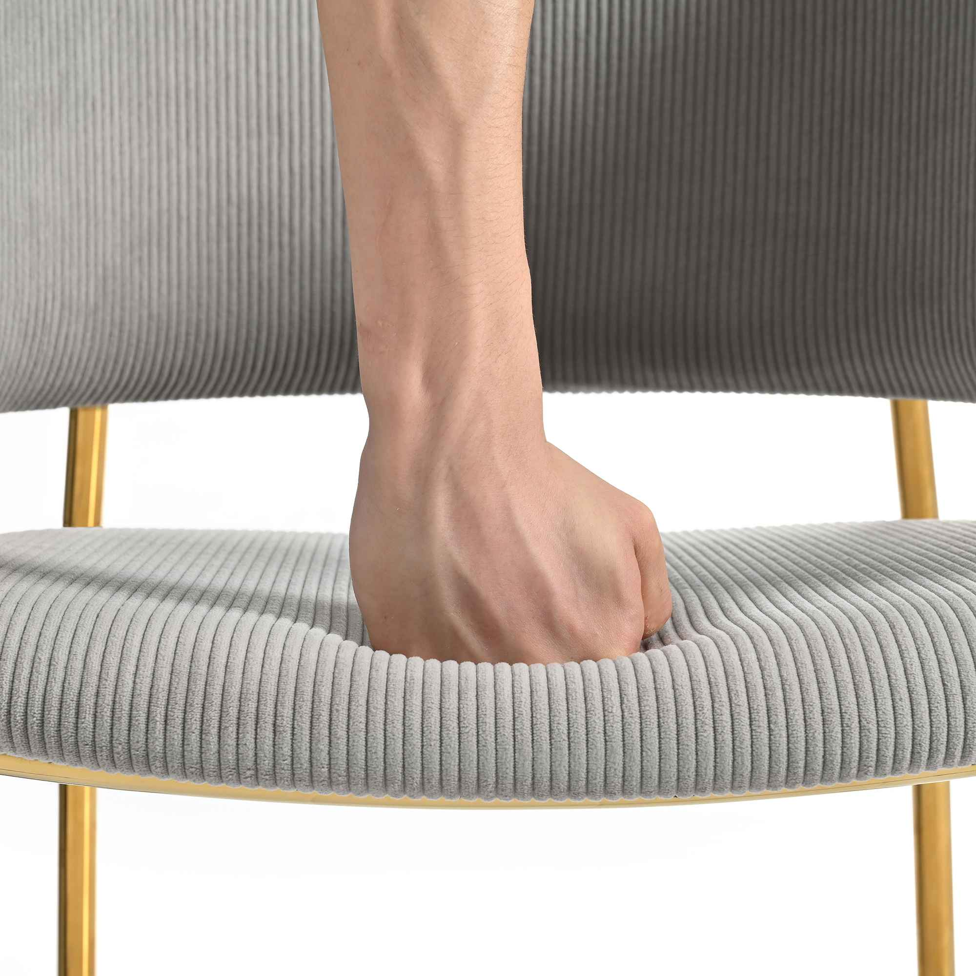 Eine Hand drückt in den grauen Sitz eines Stuhls mit goldenen Beinen, zeigt eine Vertiefung.