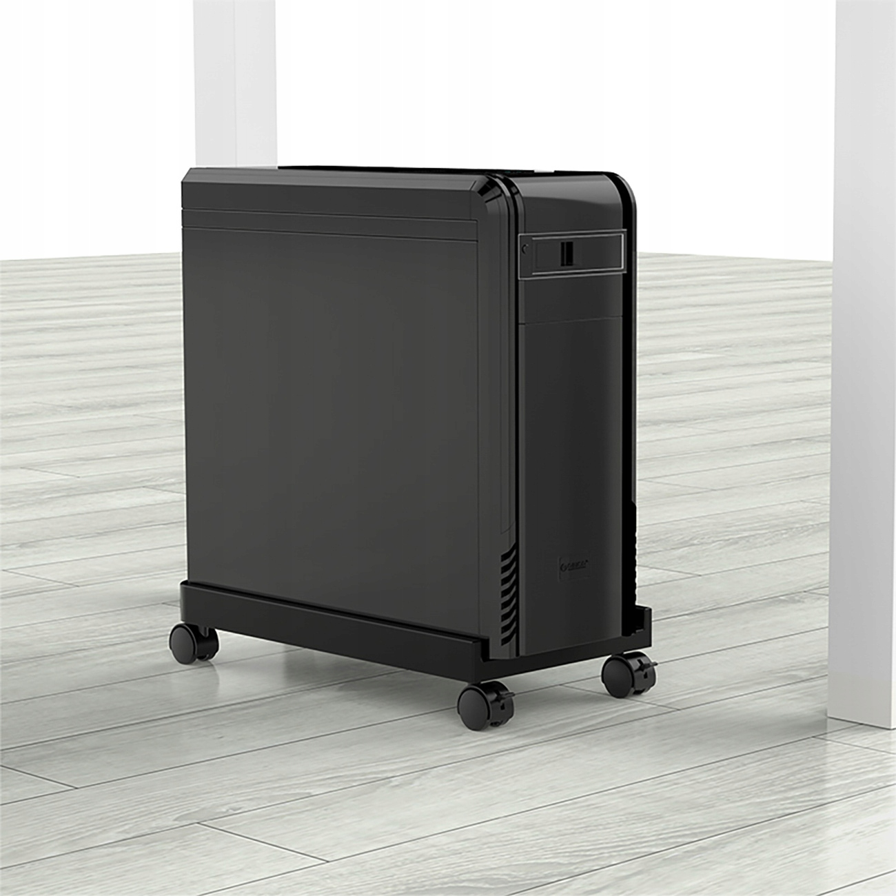 Czarna obudowa komputera na stojaku na kółkach, umieszczona na jasnej drewnianej podłodze na tle białej ściany.