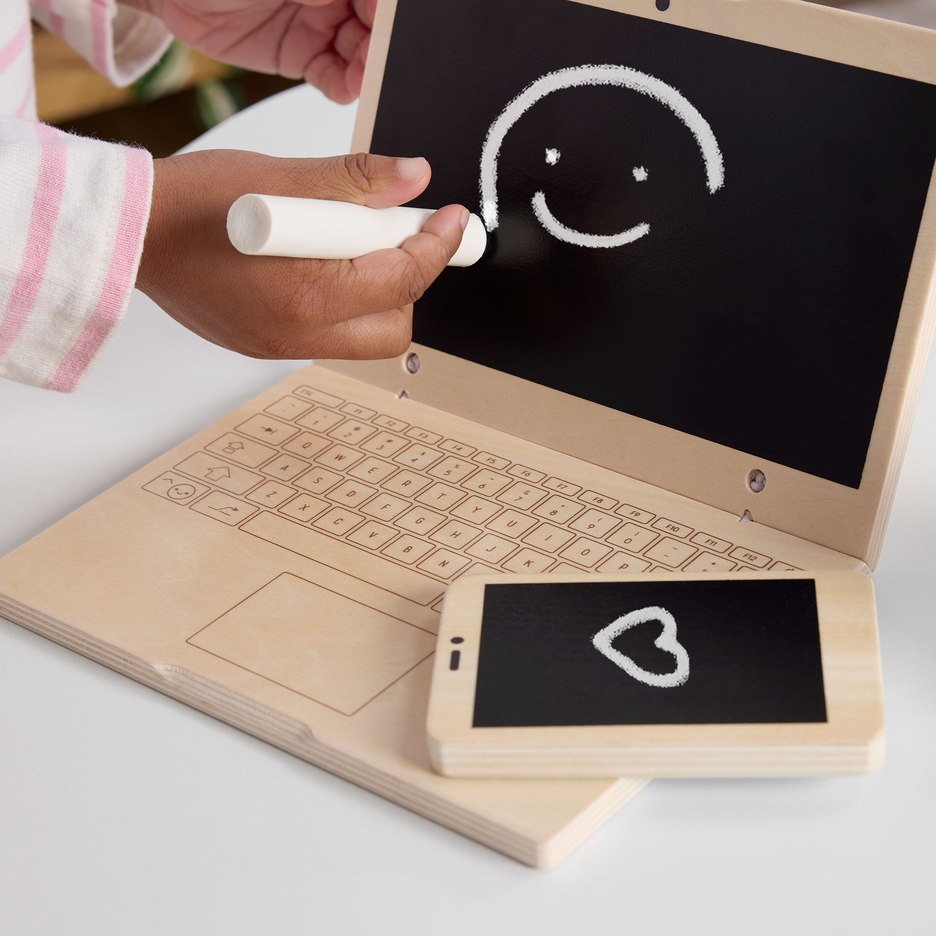 Dziecko rysuje uśmiechniętą buźkę na zabawkowym laptopie za pomocą rysika; zabawkowy telefon pokazuje serce.