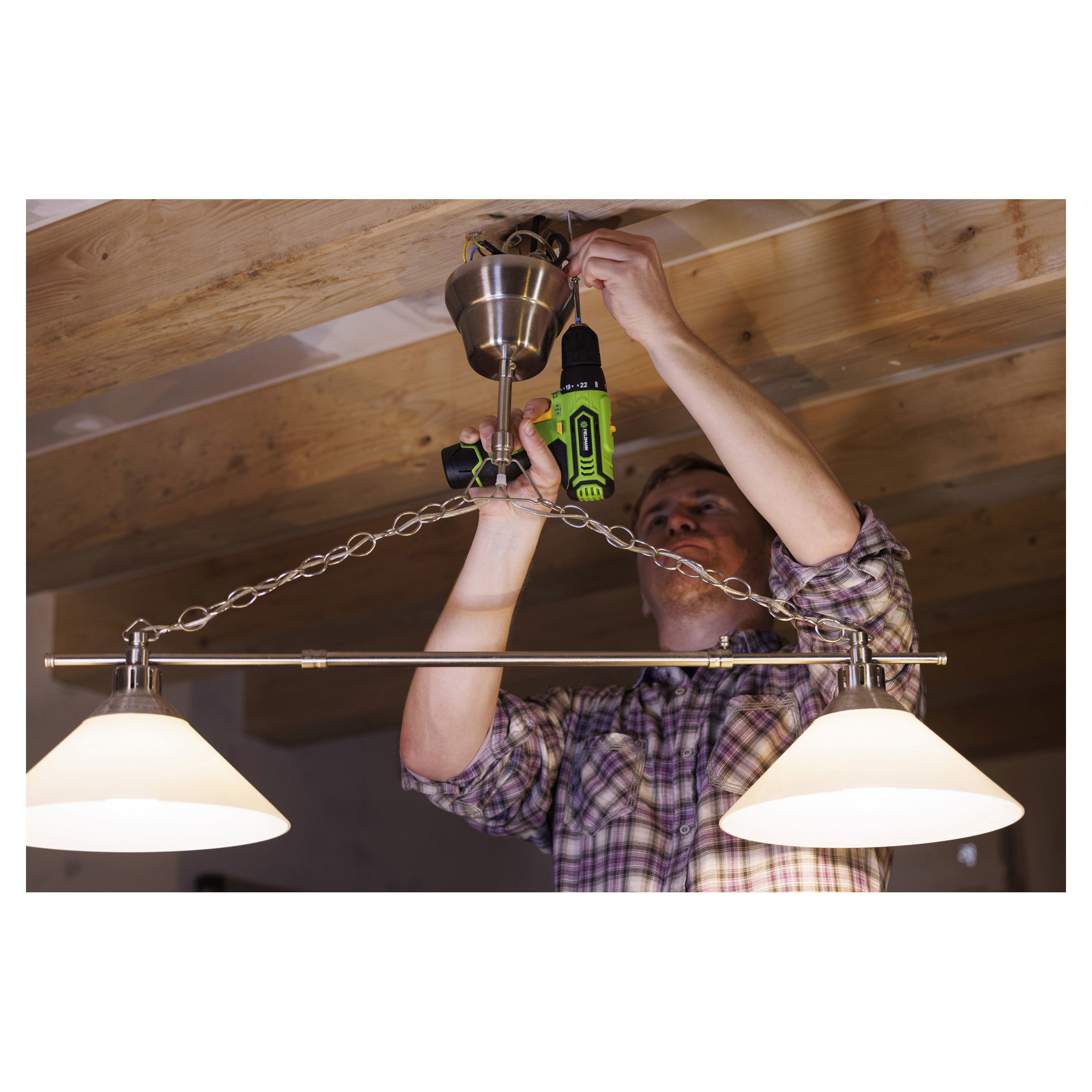 Mężczyzna instaluje lampę sufitową za pomocą wiertarki akumulatorowej.