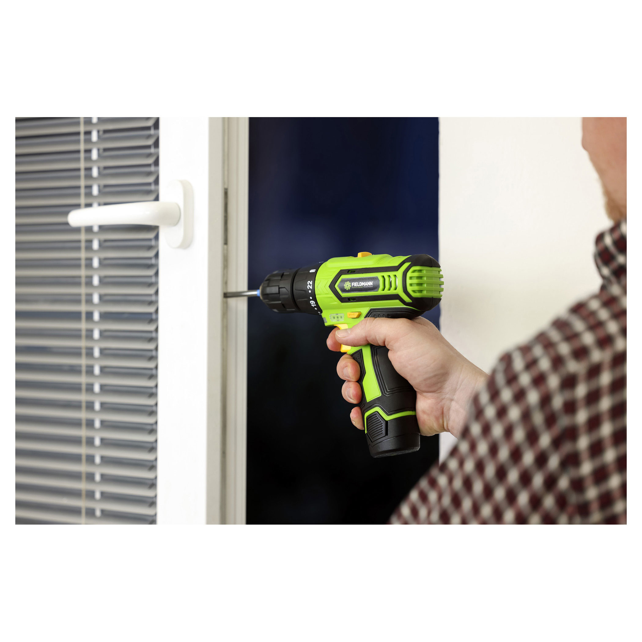 Osoba używająca zielono-czarnej wiertarki do wkręcania w białą ościeżnicę.