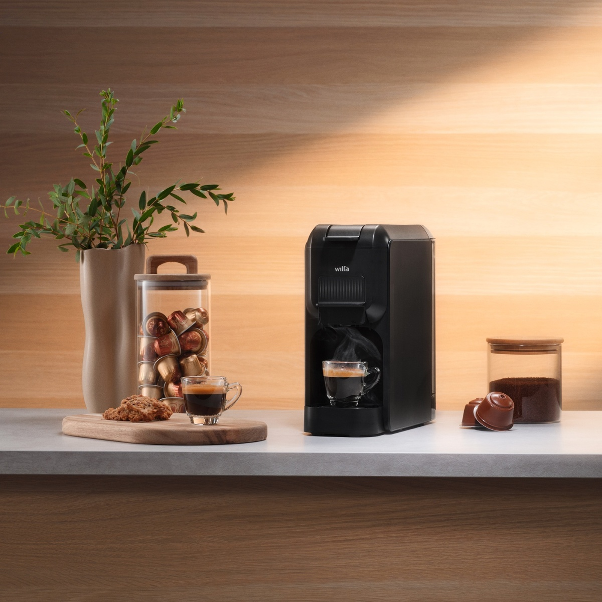 Schwarze Kaffeemaschine mit Kaffeetassen und Kapseln, mit Keksen und einer Vase.