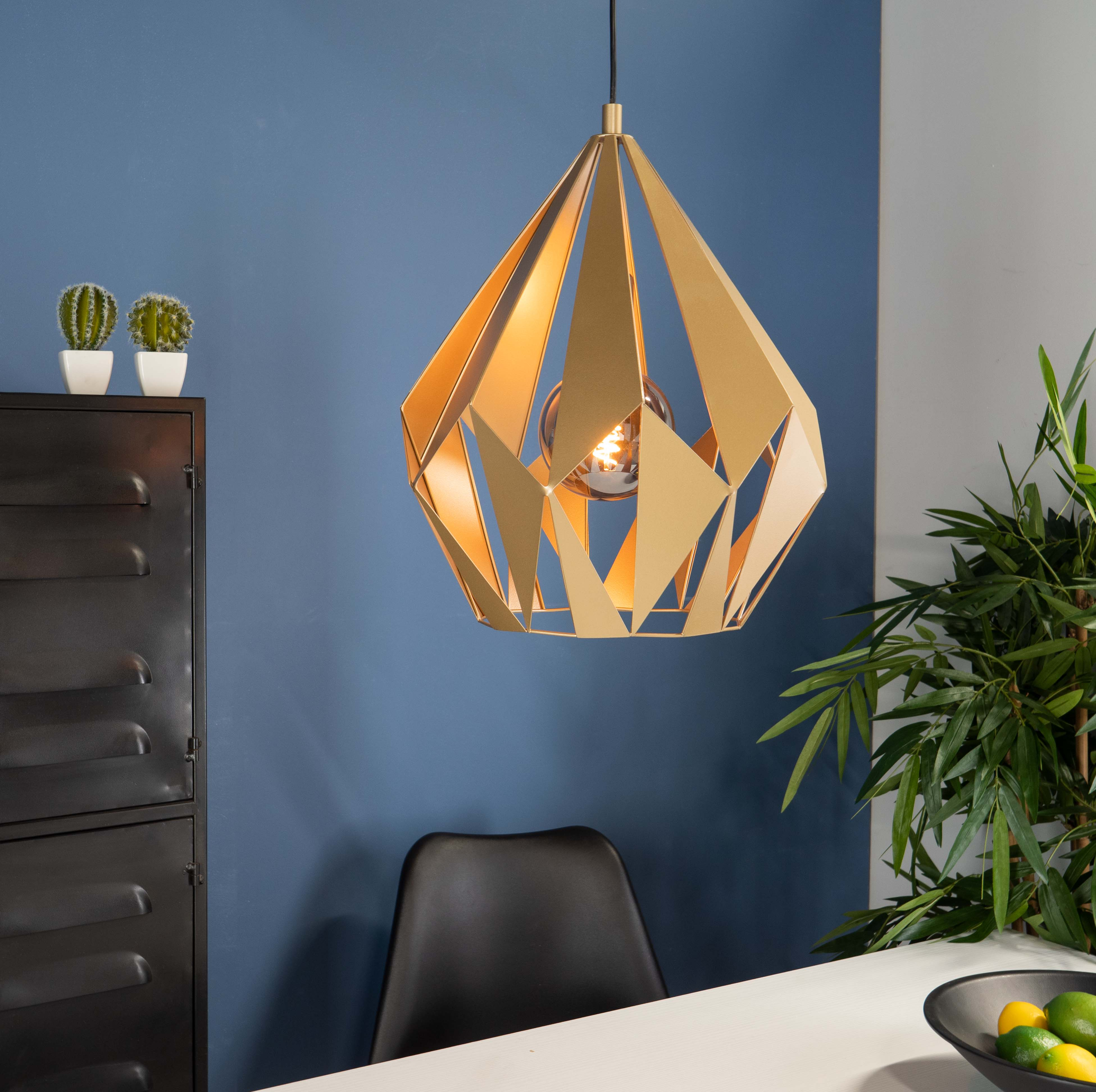 Goldene geometrische Pendelleuchte mit sichtbarer Glühbirne. Blauer Wandhintergrund mit Stuhl.