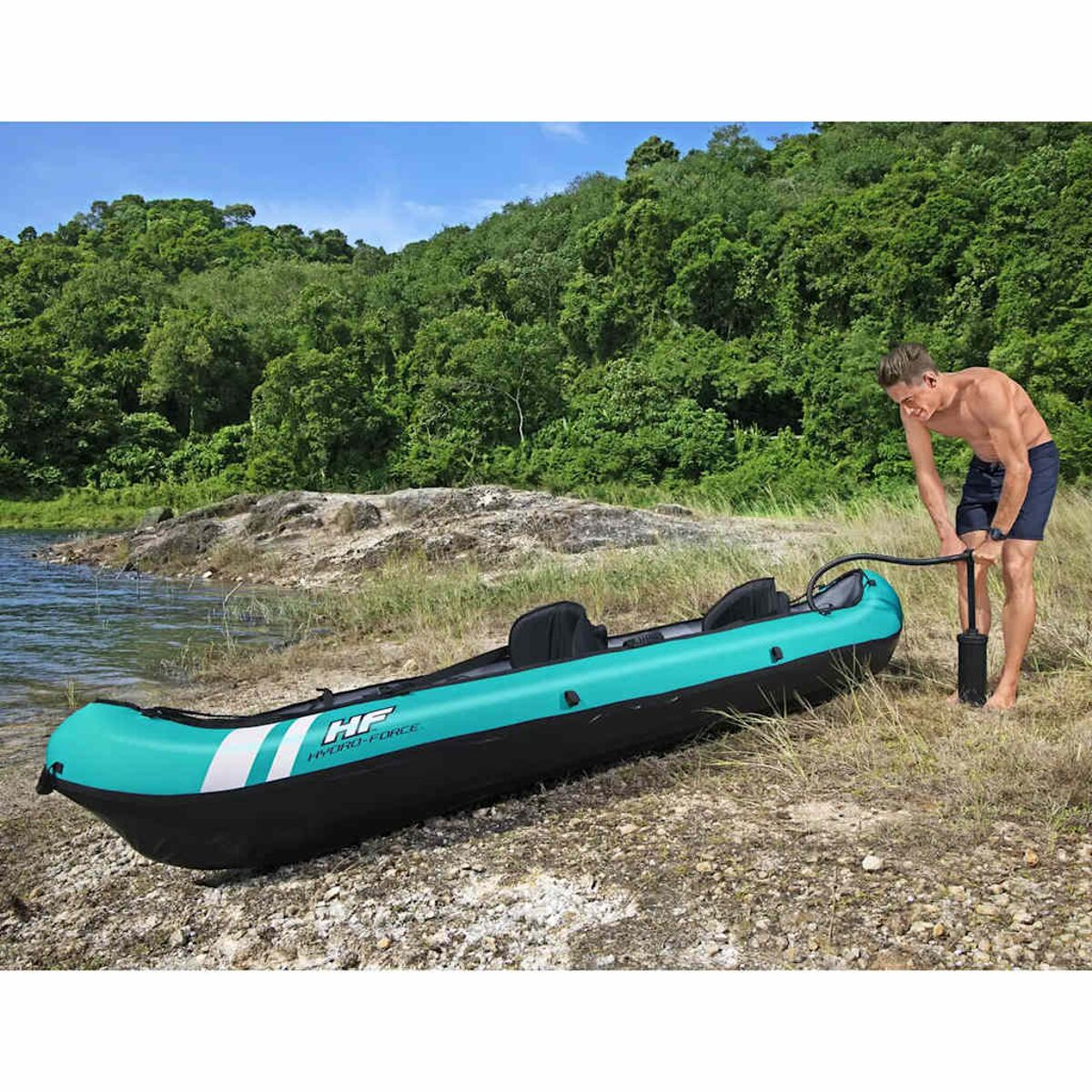 Homme gonflant un kayak turquoise et noir sur une plage. Arbres verts en arrière-plan.